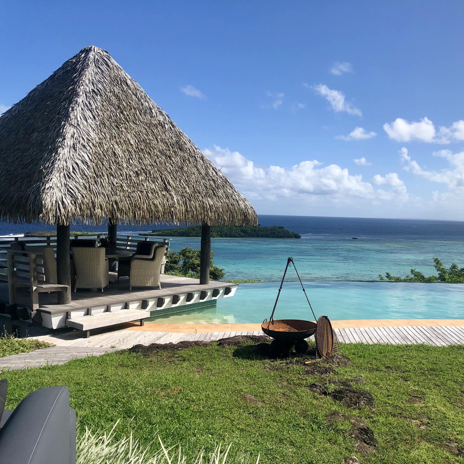 A straw hut cabana and infinity pool in front of expansive ocean views.