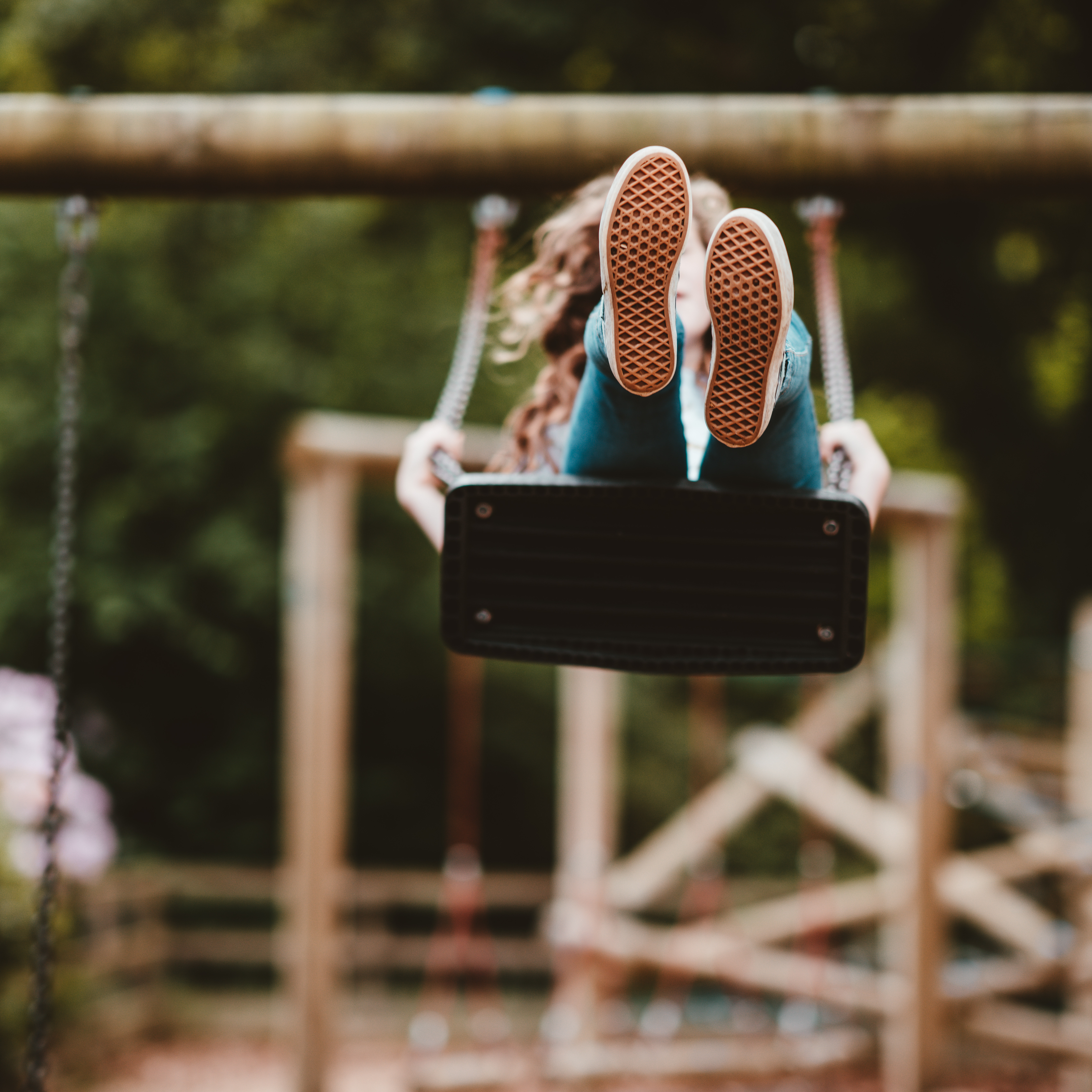 Child swinging on playground swing with feet facing forward with a blurred background play area