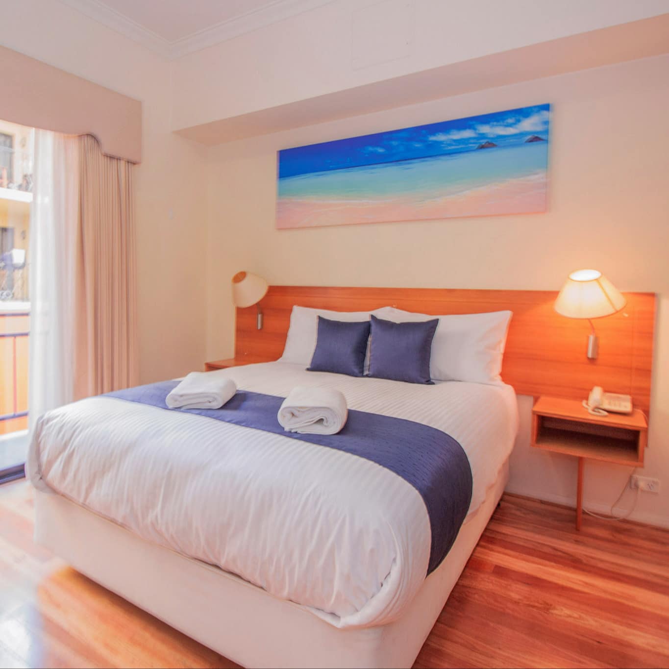 Bedroom with hardwood floors, a king size bed, white and blue bedding, and sliding glass doors to balcony.