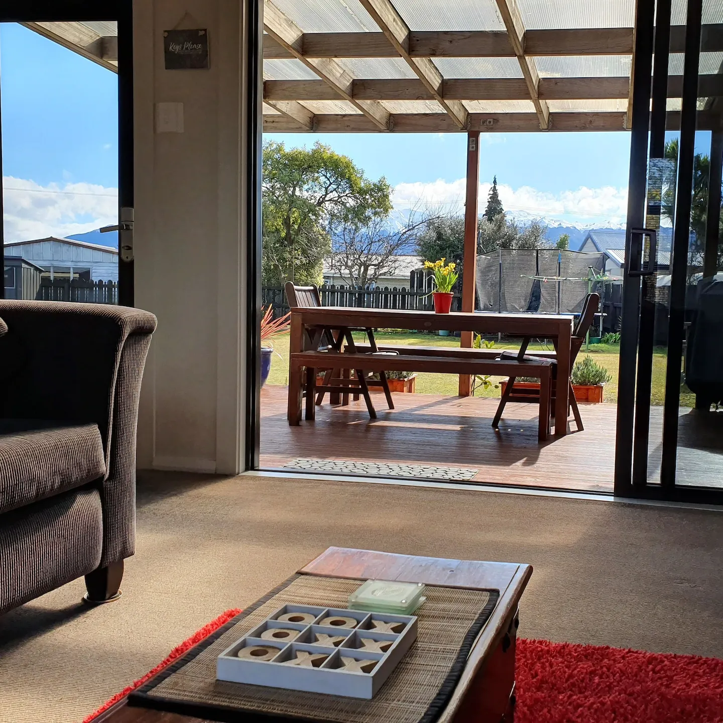 The living room of a holiday home with an open glass door revealing a deck with a table and the mountains in the distance