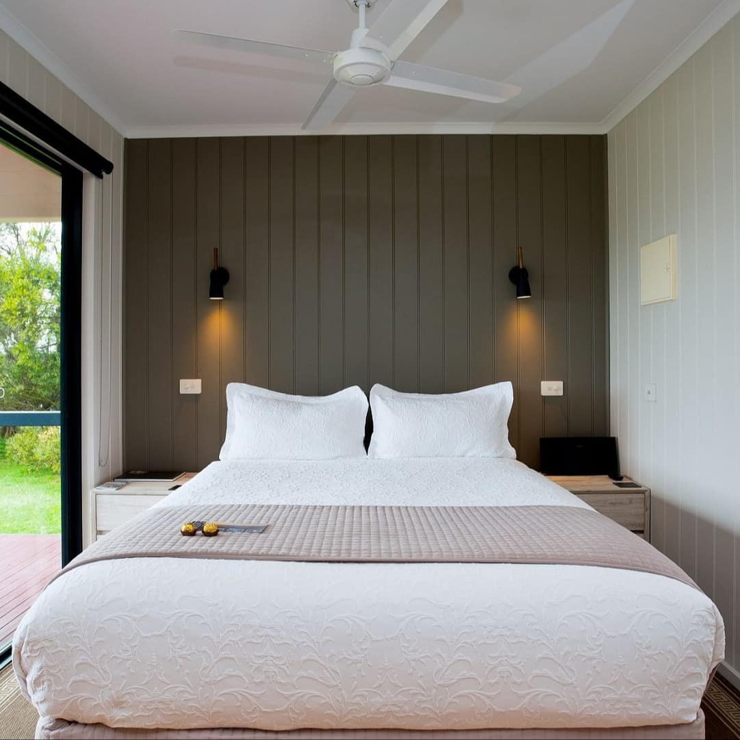 Bedroom with a queen size bed, white and beige bedding, white and dark green panelled walls, wide window.