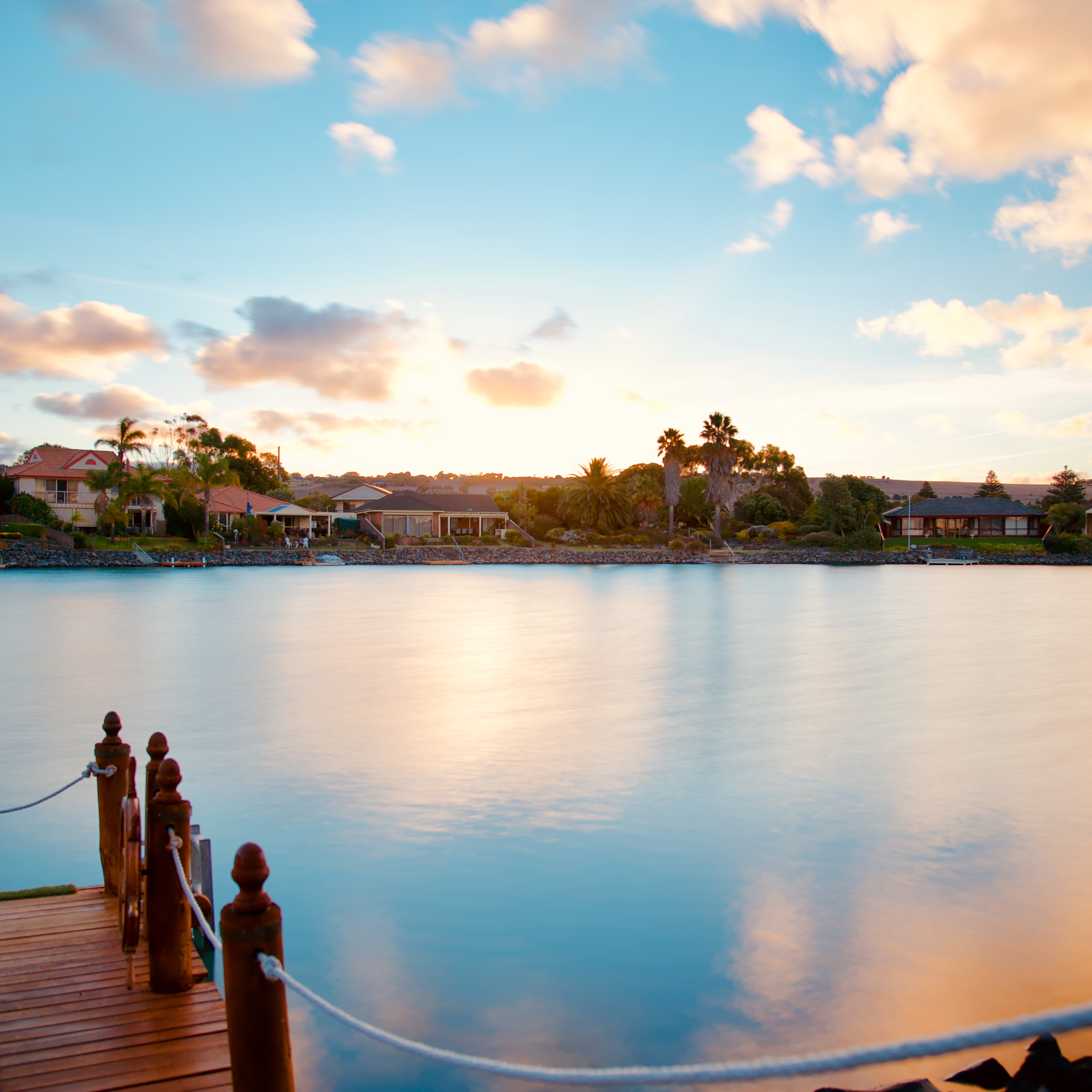 A view across Encounter Bay in Adelaide at sunrise with peach and blue reflections on the water and villas on the shore