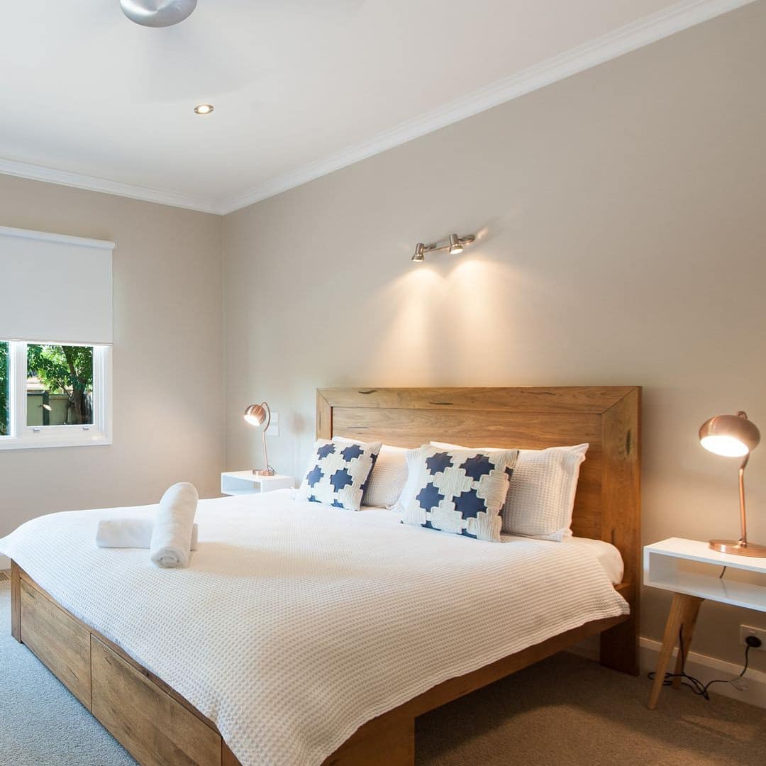 Spacious bedroom with beige carpet and walls, wood-framed king size bed, white and navy blue bedding, wide window.
