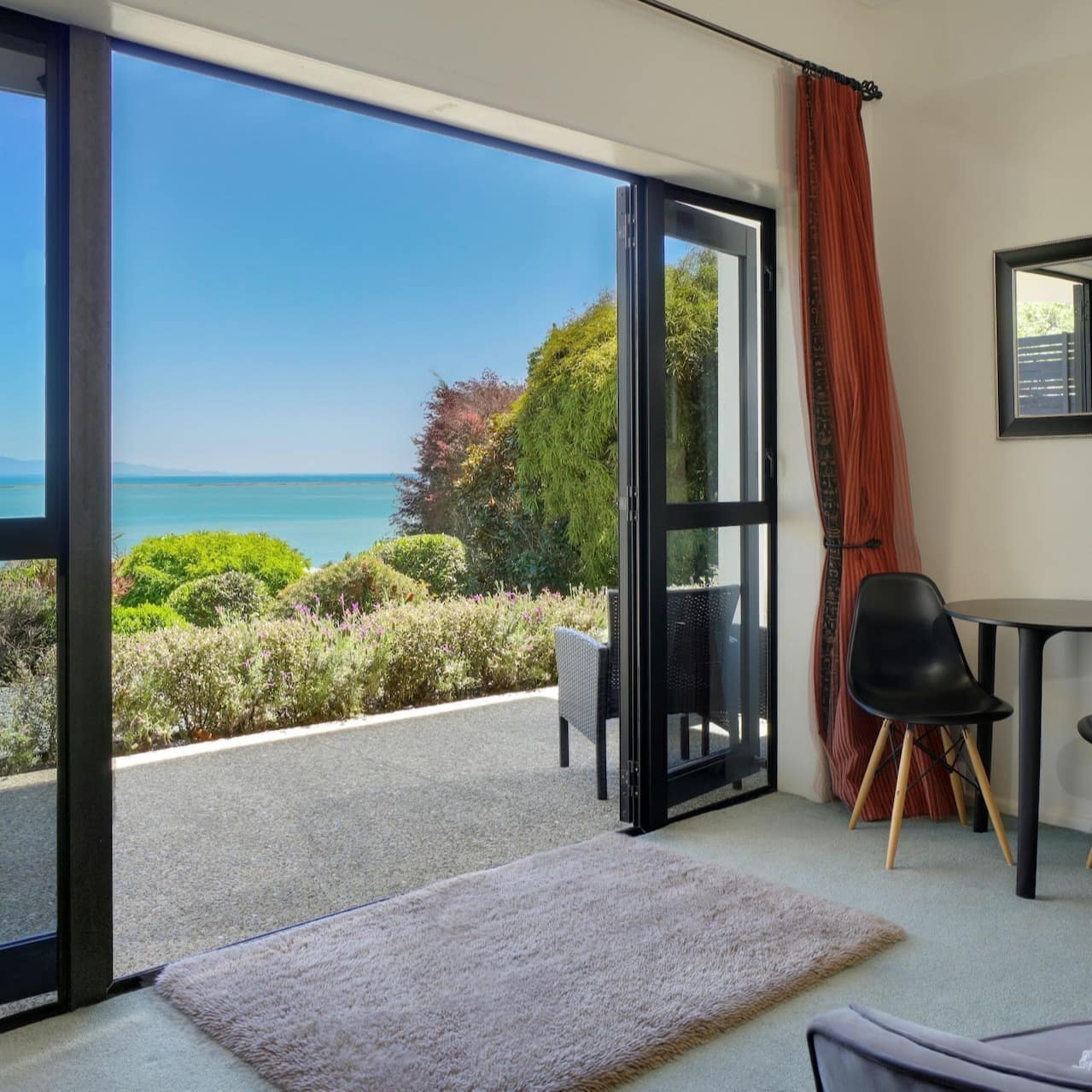 A modernly-furnished living room looking out through open glass doors onto clear blue waters