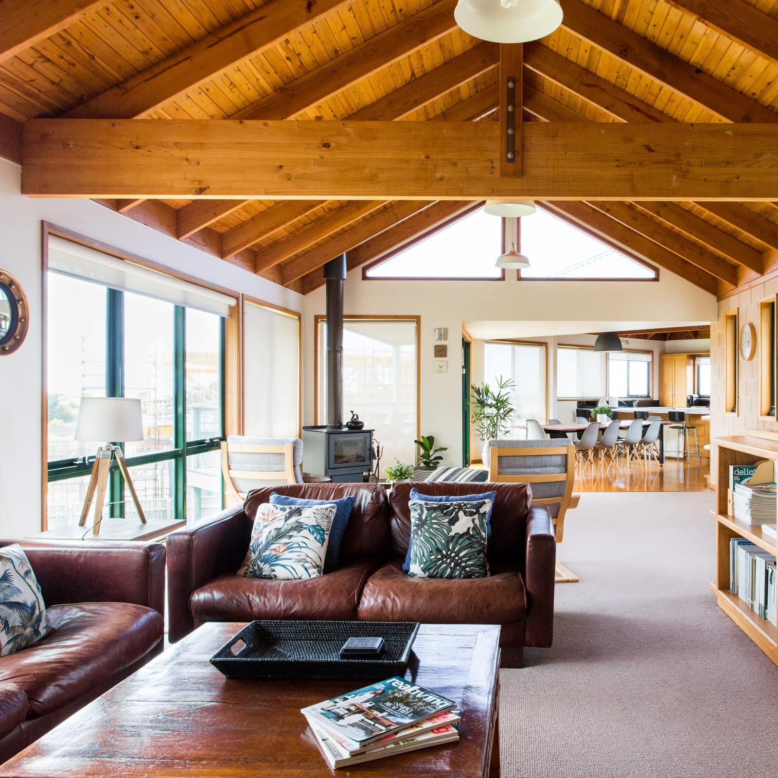 Open living room with vaulted ceilings and exposed wood beams, brown leather sofas, and wooden coffee table.