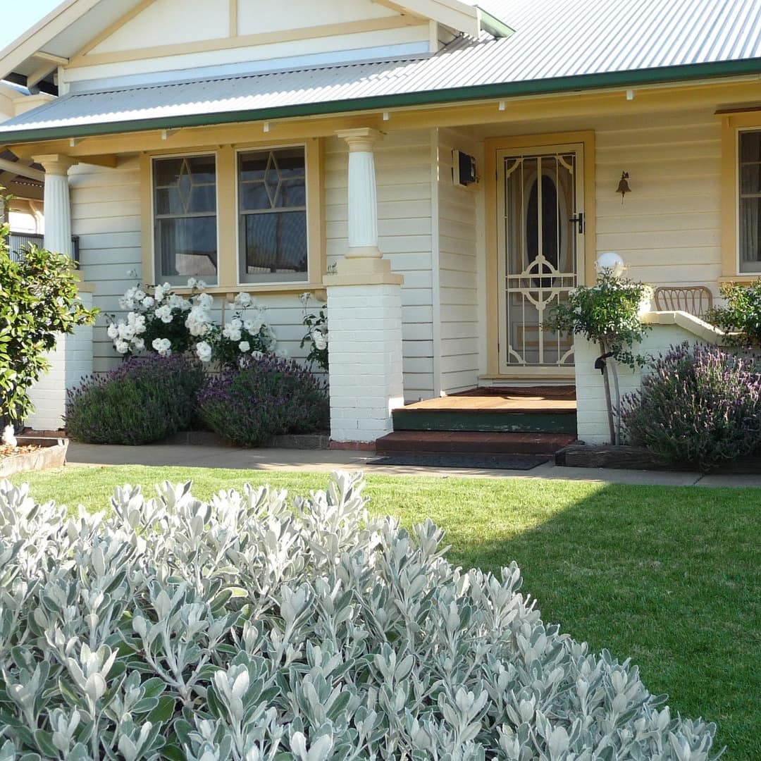 White cottage with yellow trim, covered porch, landscape lawn.