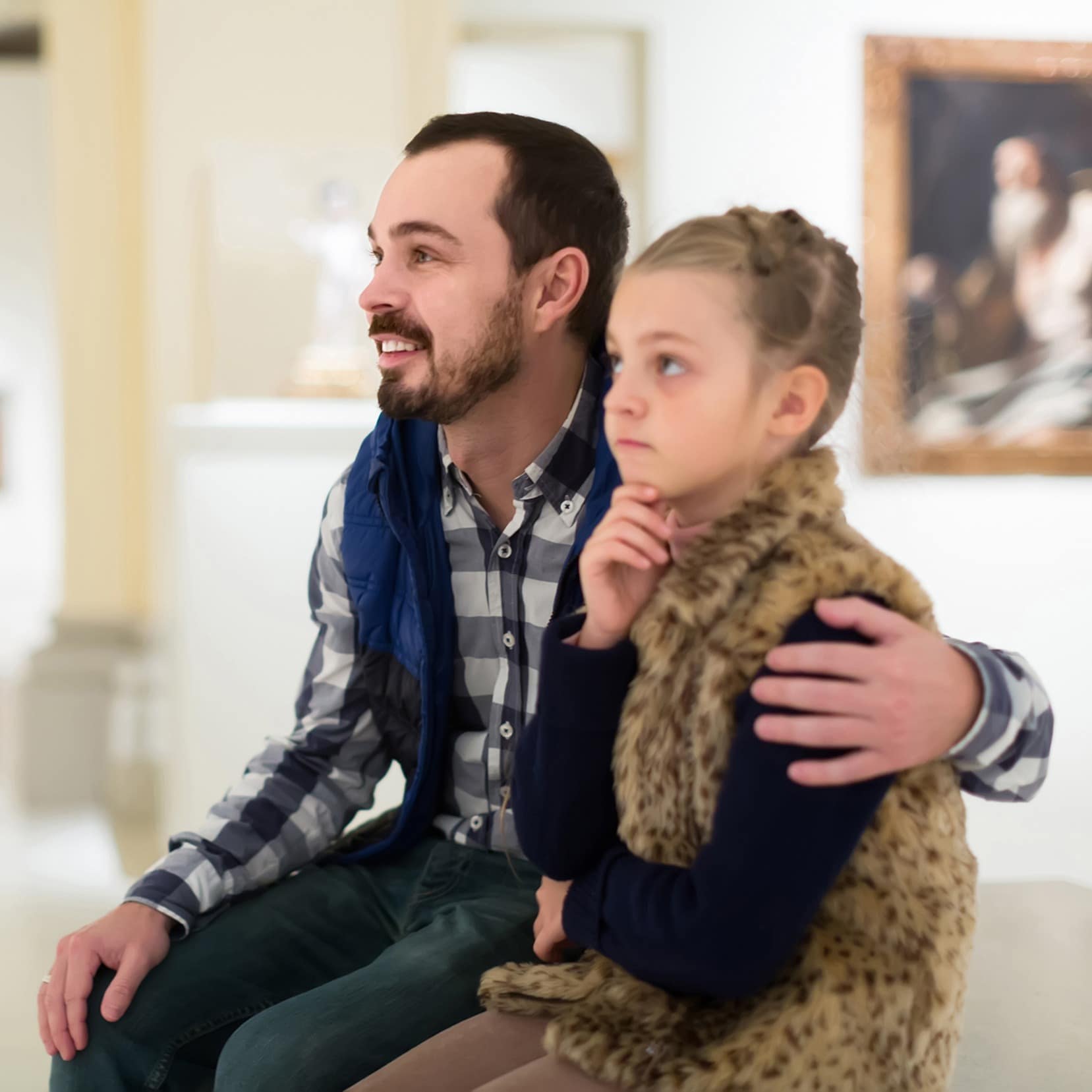 Smiling father and daughter study paintings in halls of museum