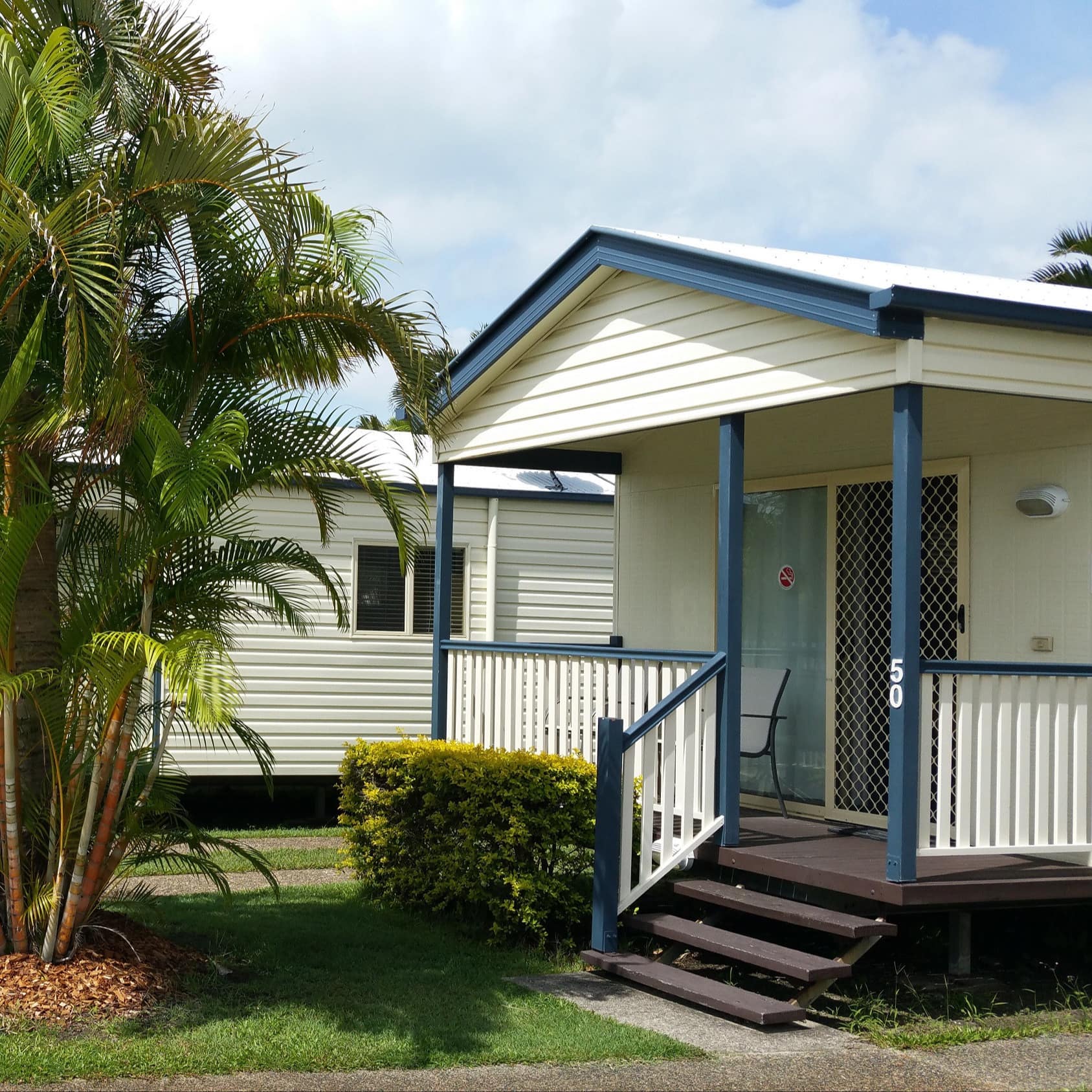 Exterior of 2-bedroom beach cabin, white with blue trim and small front porch overlooking front yard with palm tree