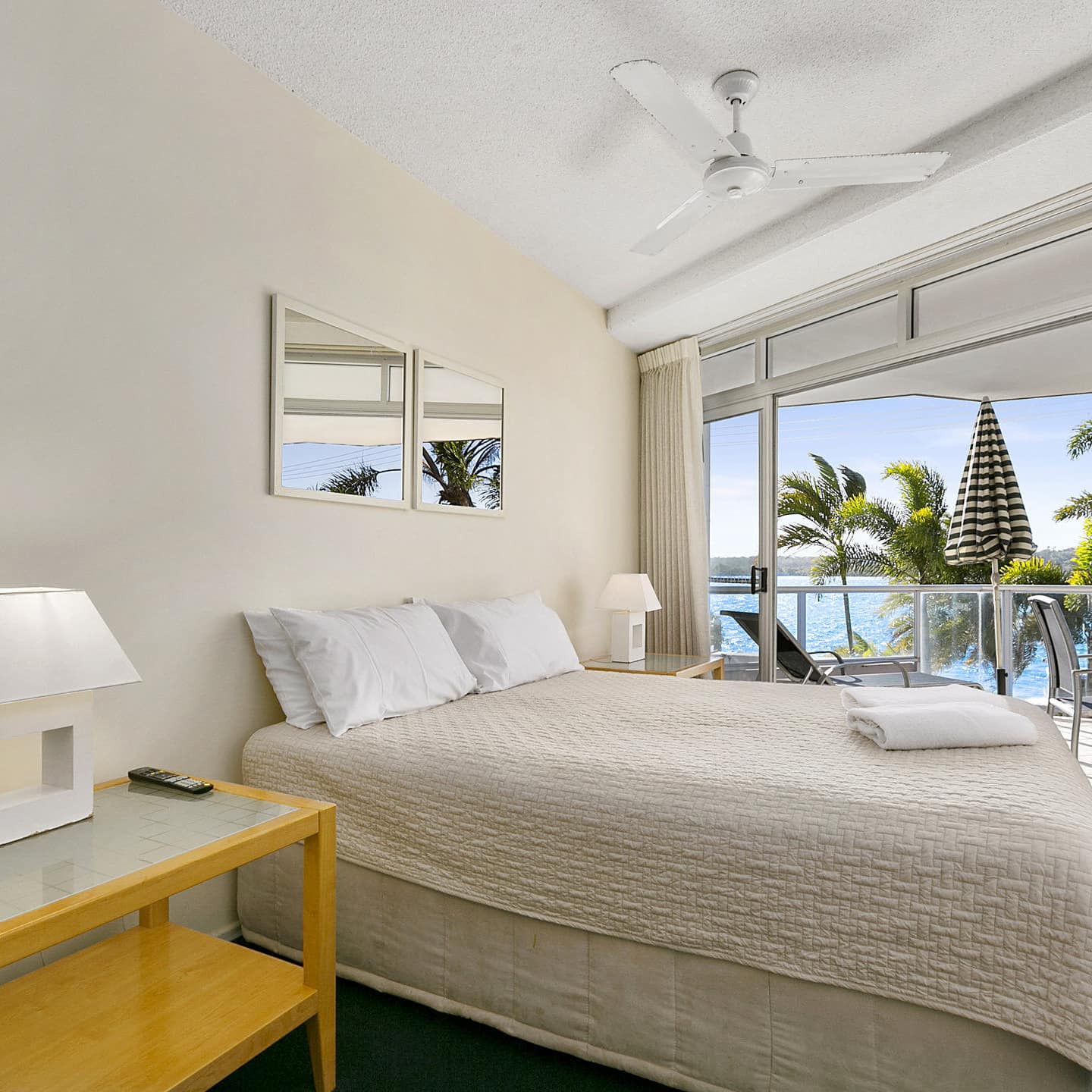 Bedroom with a queen size bed, beige bedding and walls, matching wood bedside tables, attached balcony with ocean views.