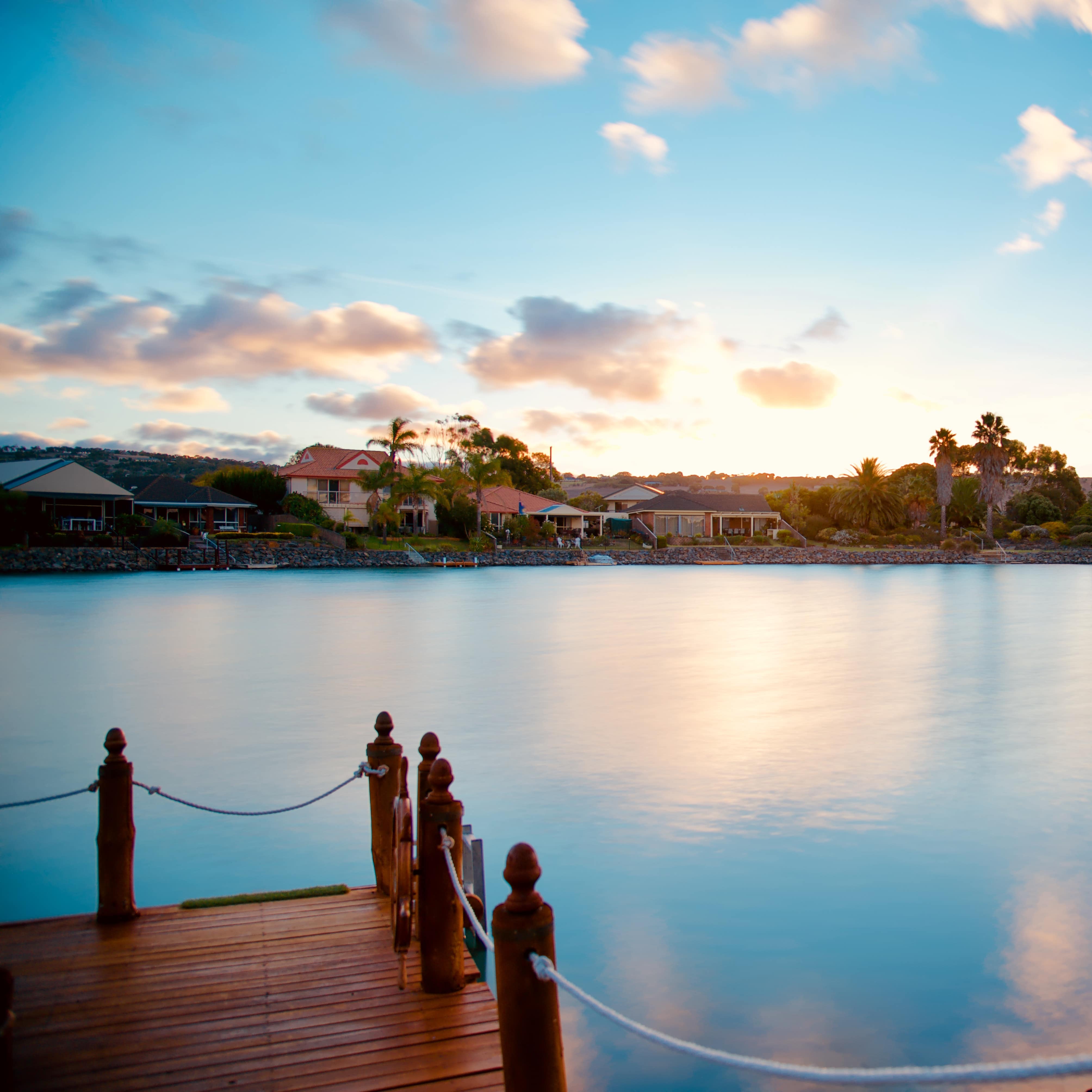 A view across Encounter Bay in Adelaide at sunrise with peach and blue reflections on the water and villas on the shore