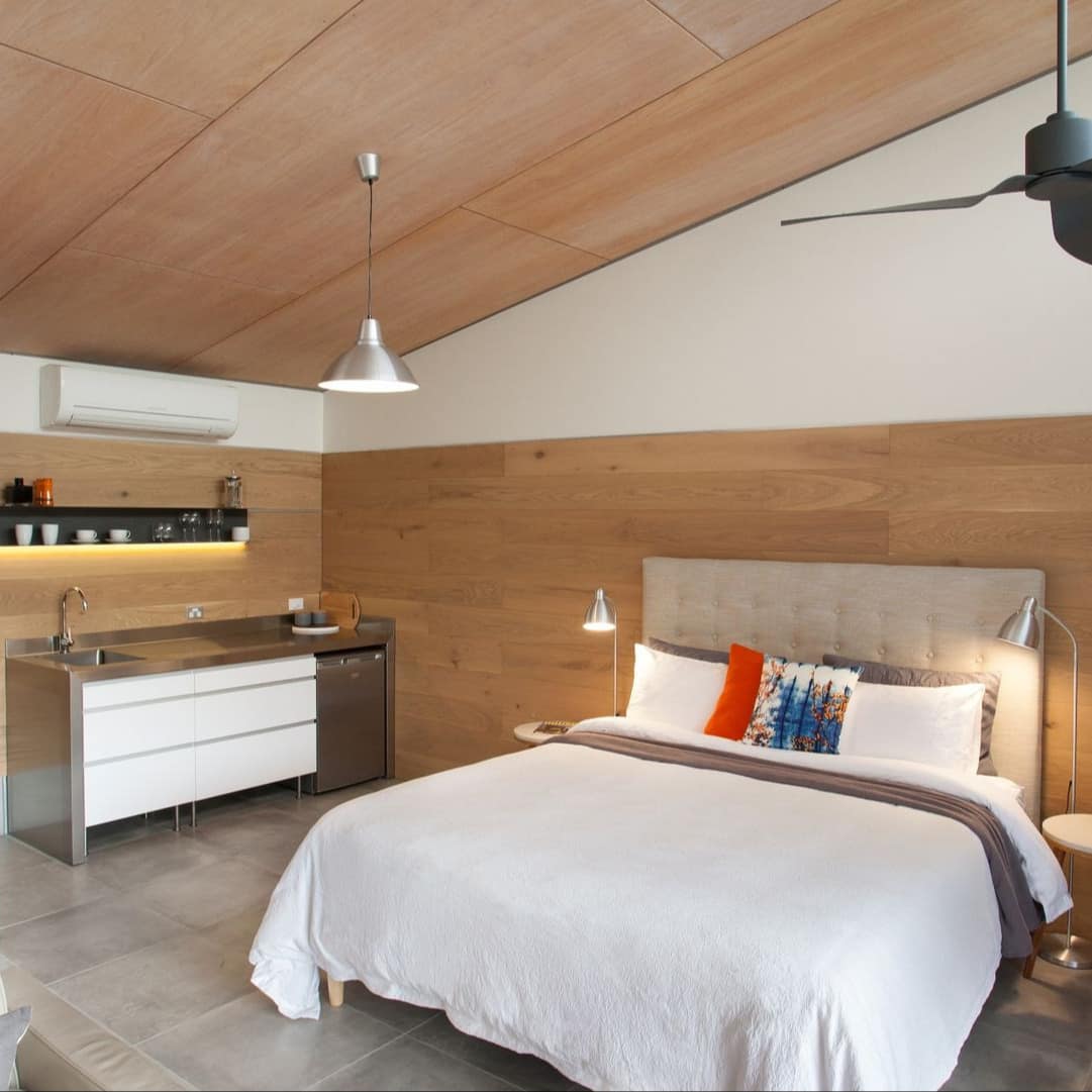 Studio space with a king-size bed, white and brown bedding, a kitchenette, grey tile floors, and wood-panelled walls.