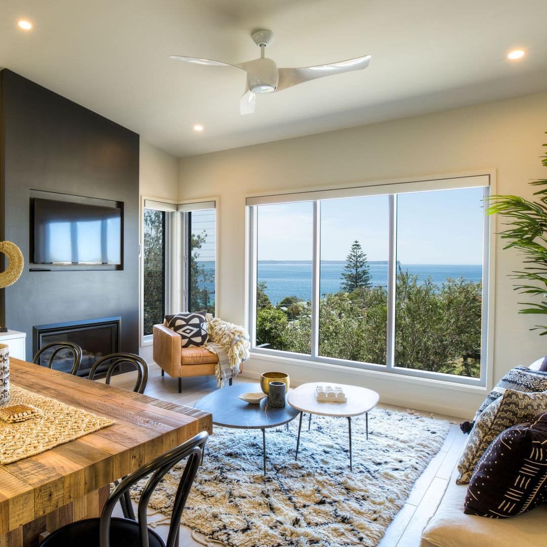 Interior of beach townhouse with open living and dining room with windows on two sides of the room and soft cloth sofa