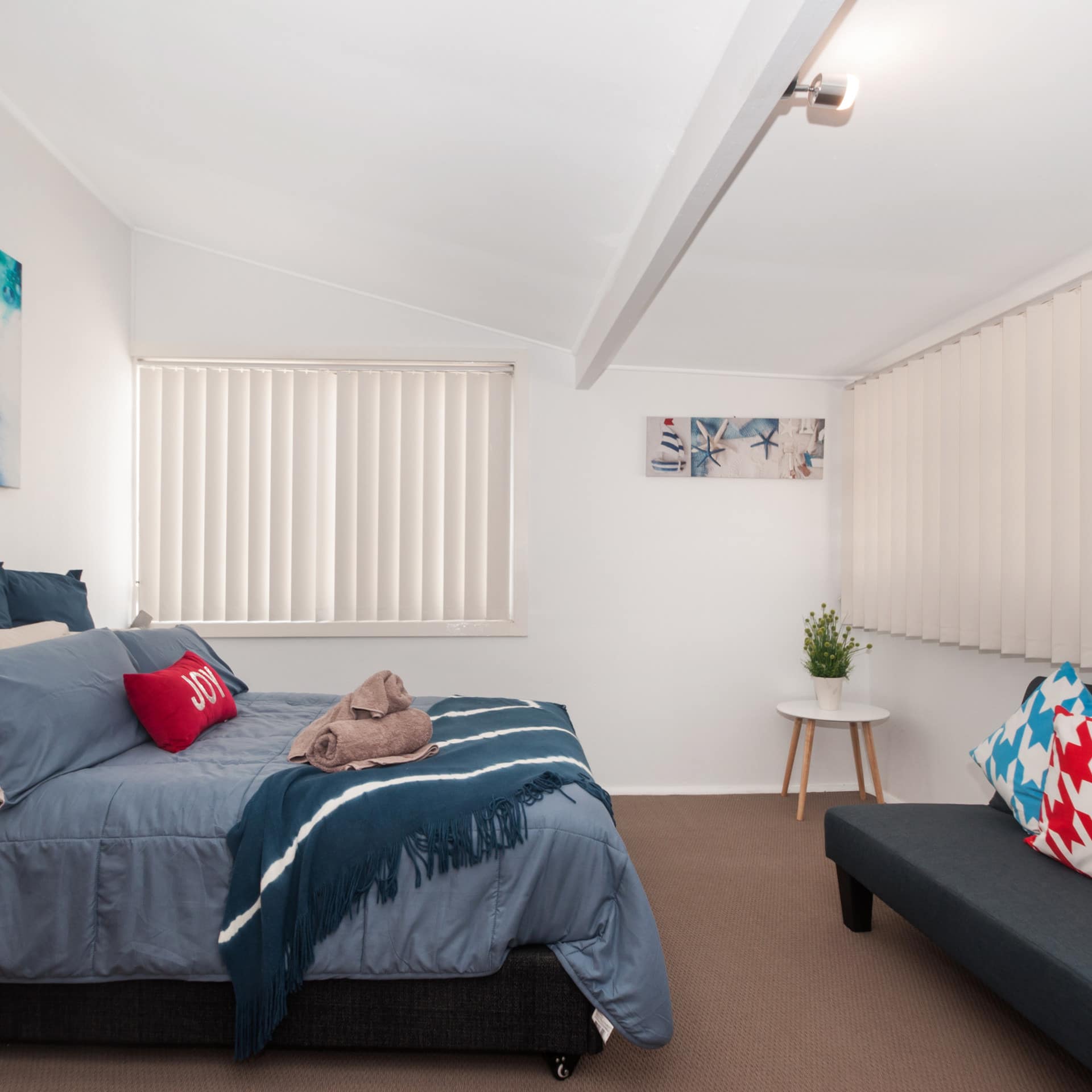 Spacious bedroom with a king-size bed, blue bedding, grey canvas sofa, and white bookshelves with wicker baskets.