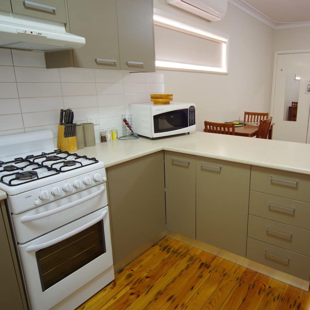Open kitchen with hardwood floors, white tile backsplash, green cabinets, white countertops, and white appliances.