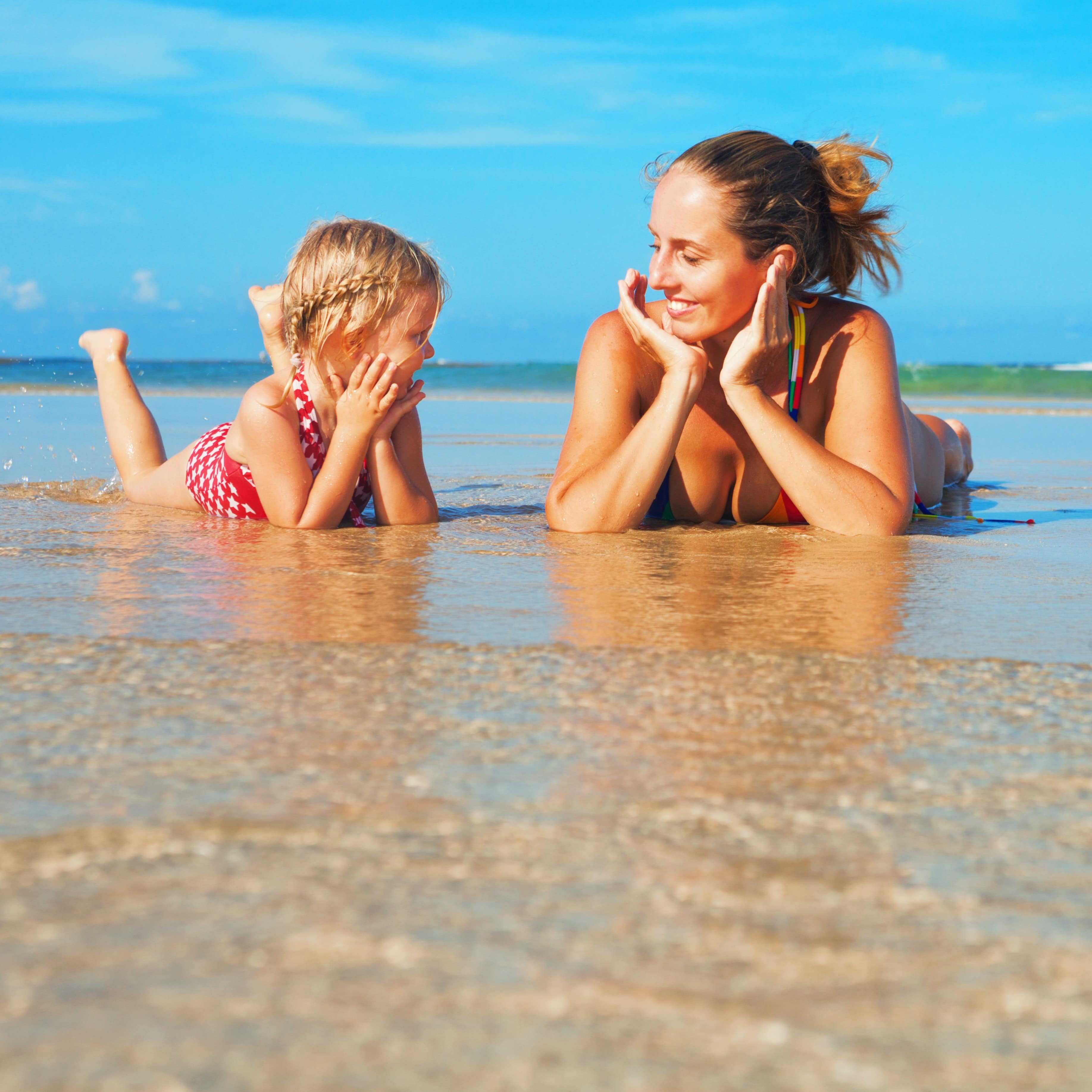 Young mother with a child lying in the water at the beach looking at each other