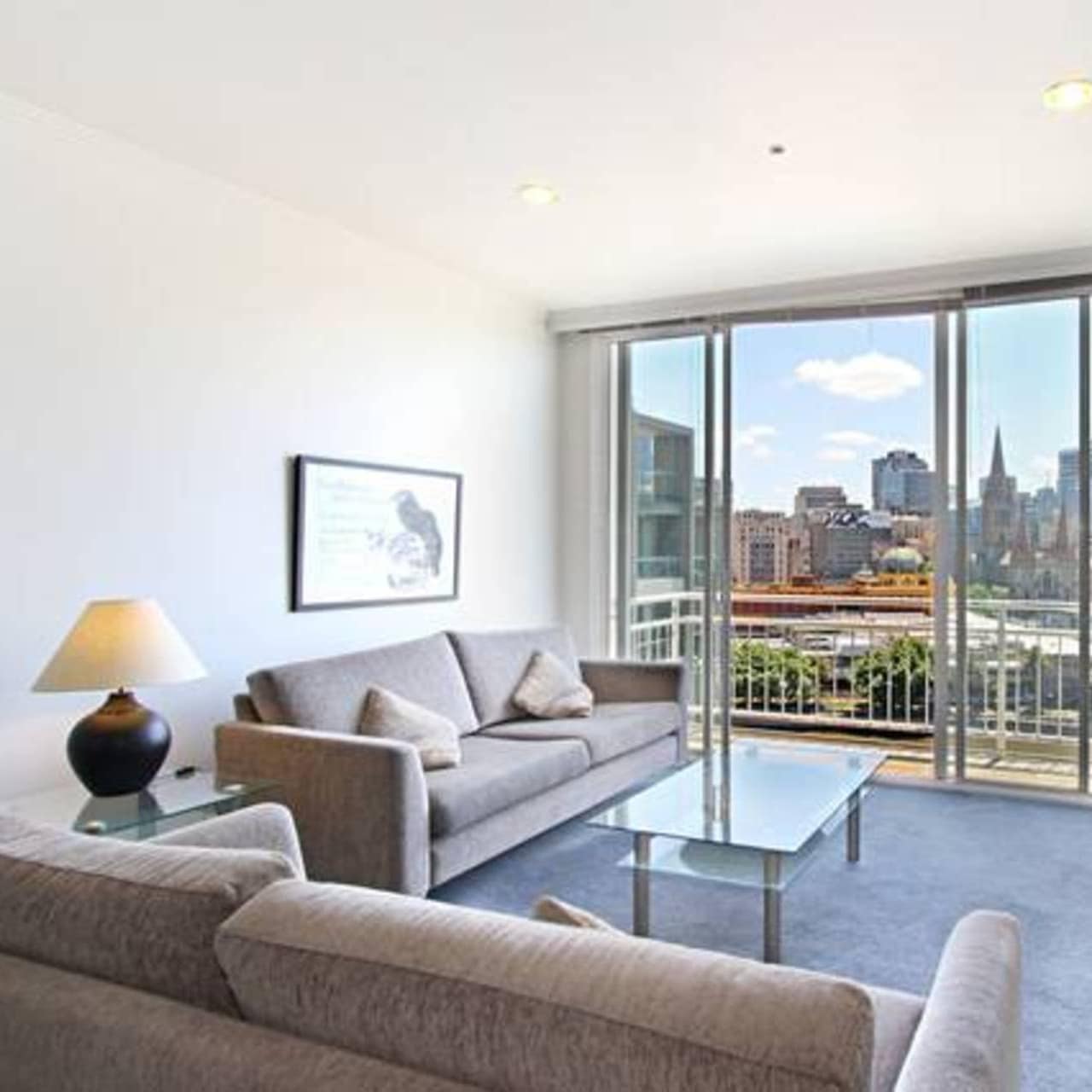 Modern living room with grey sofas, glass tables, sliding glass doors to attached balcony.
