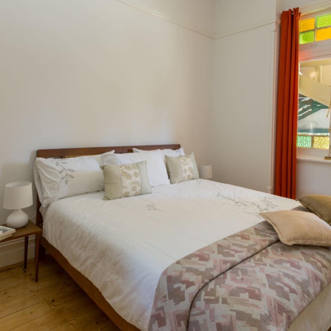 Queen bed in 3-bedroom cottage, hardwood floors and red curtains framing windows with stained glass