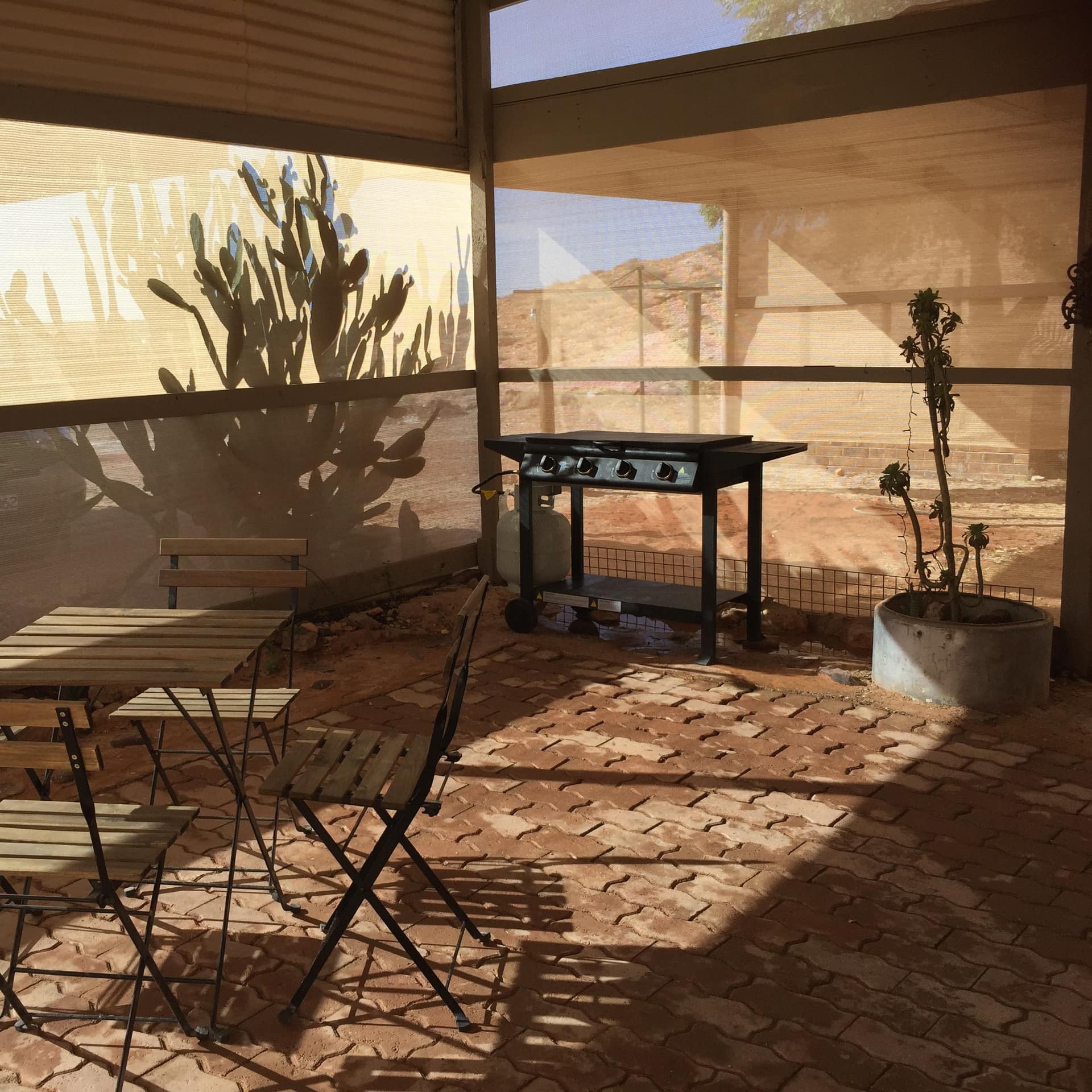Screened porch with brick floors, wooden dining set, grill, and potted plants.