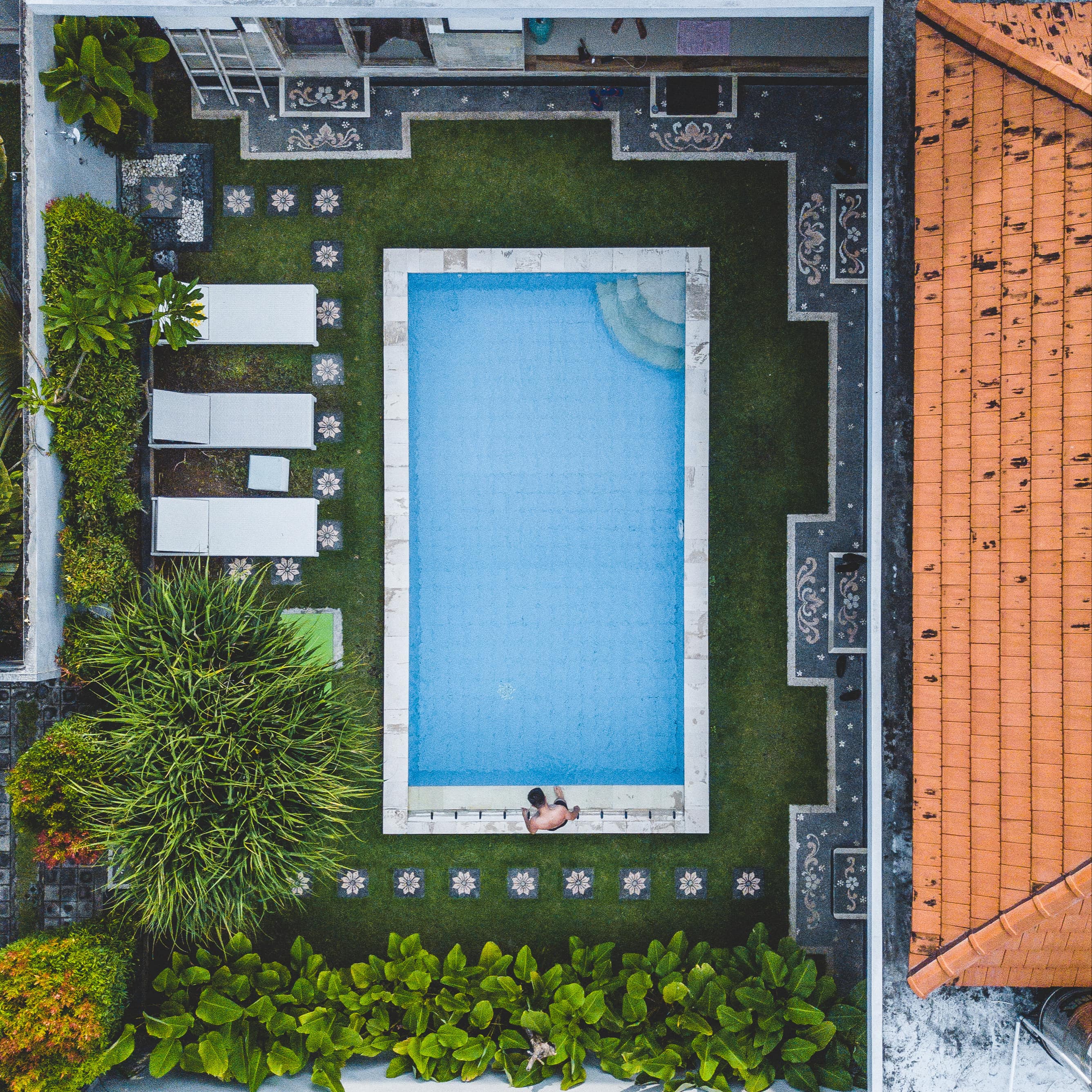 Aerial view of Seminyak villa with red tile roof, mosaic patio, rectangular pool and lounge chairs in the private courtyard