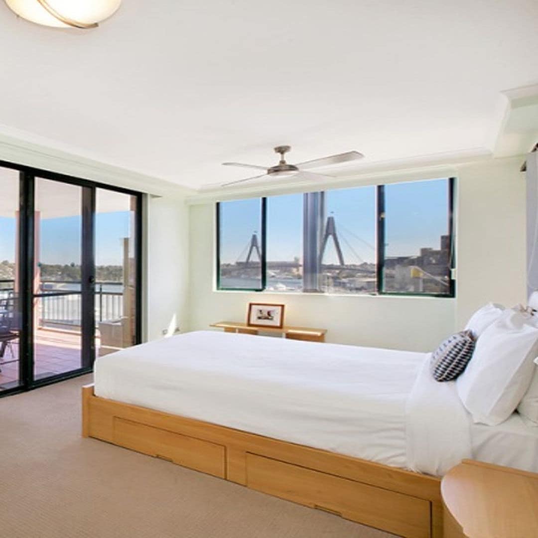 Open bedroom with light green walls, beige carpet, wood-framed king size bed, white bedding and attached balcony.