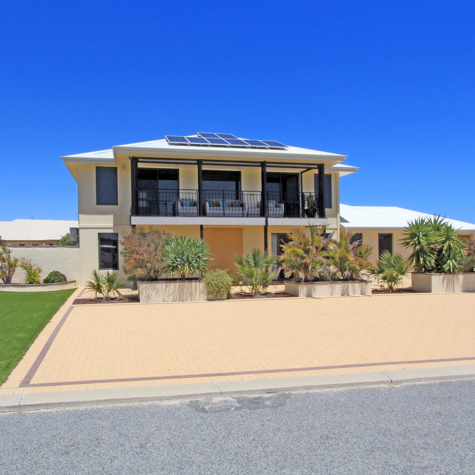Two-story home with beige siding, a second-story covered porch, beige tile driveway and landscaped lawn.