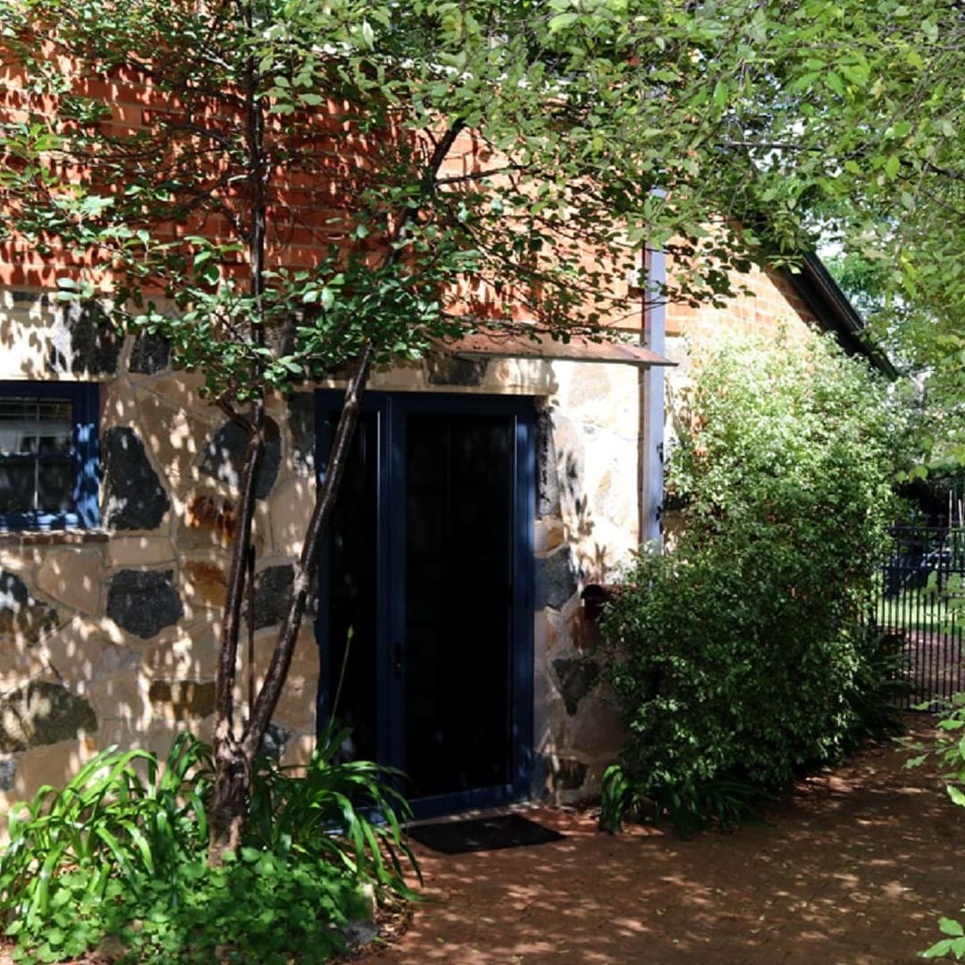 Exterior of ground floor apartment with natural stone siding, a brick pathway, and lush green courtyard.