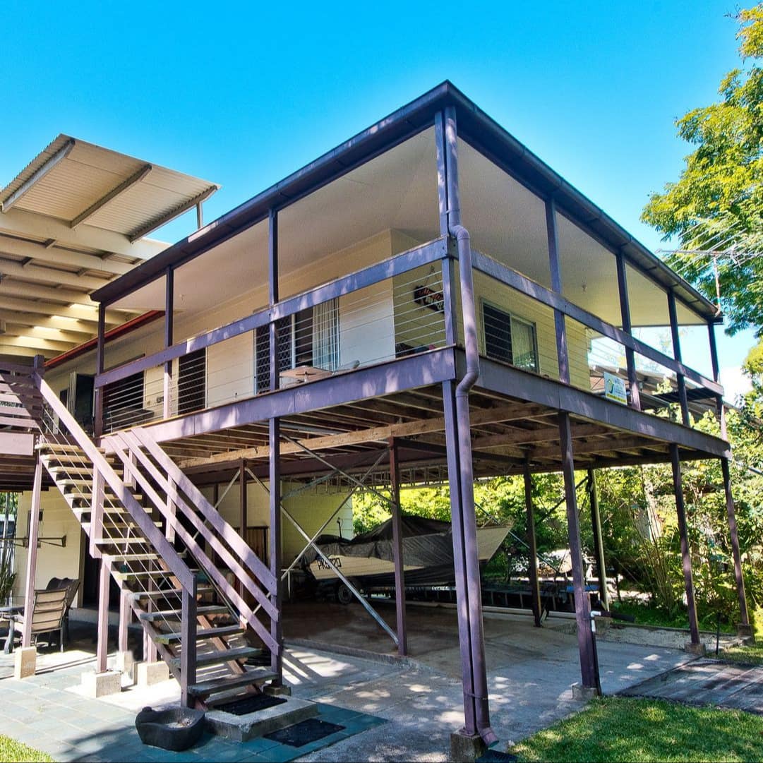 Modern, raised home with white walls and wood trim, wrap around covered porch, patio space on the ground floor.