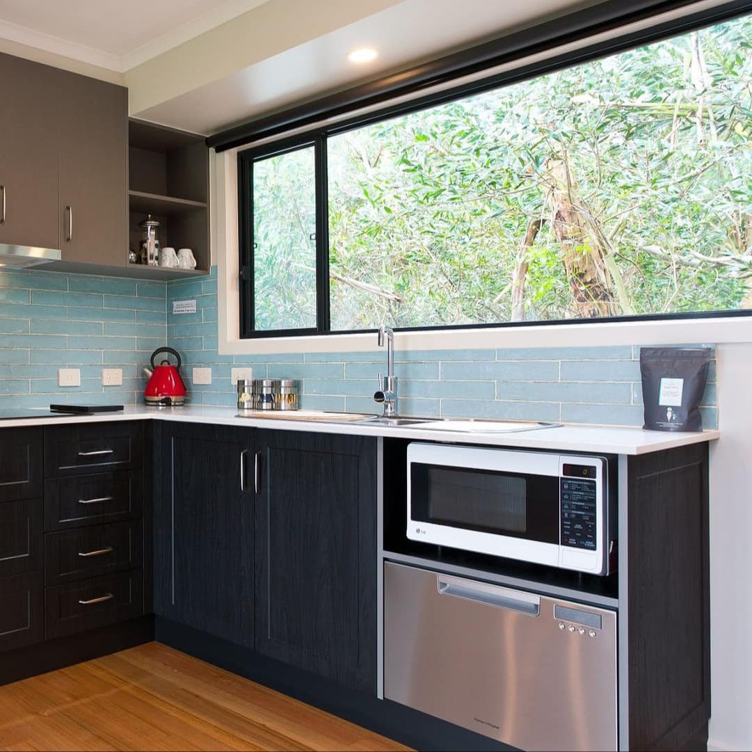 Modern kitchen with hardwood floors, black cabinets, white countertops, stainless steel appliances, and wide windows.
