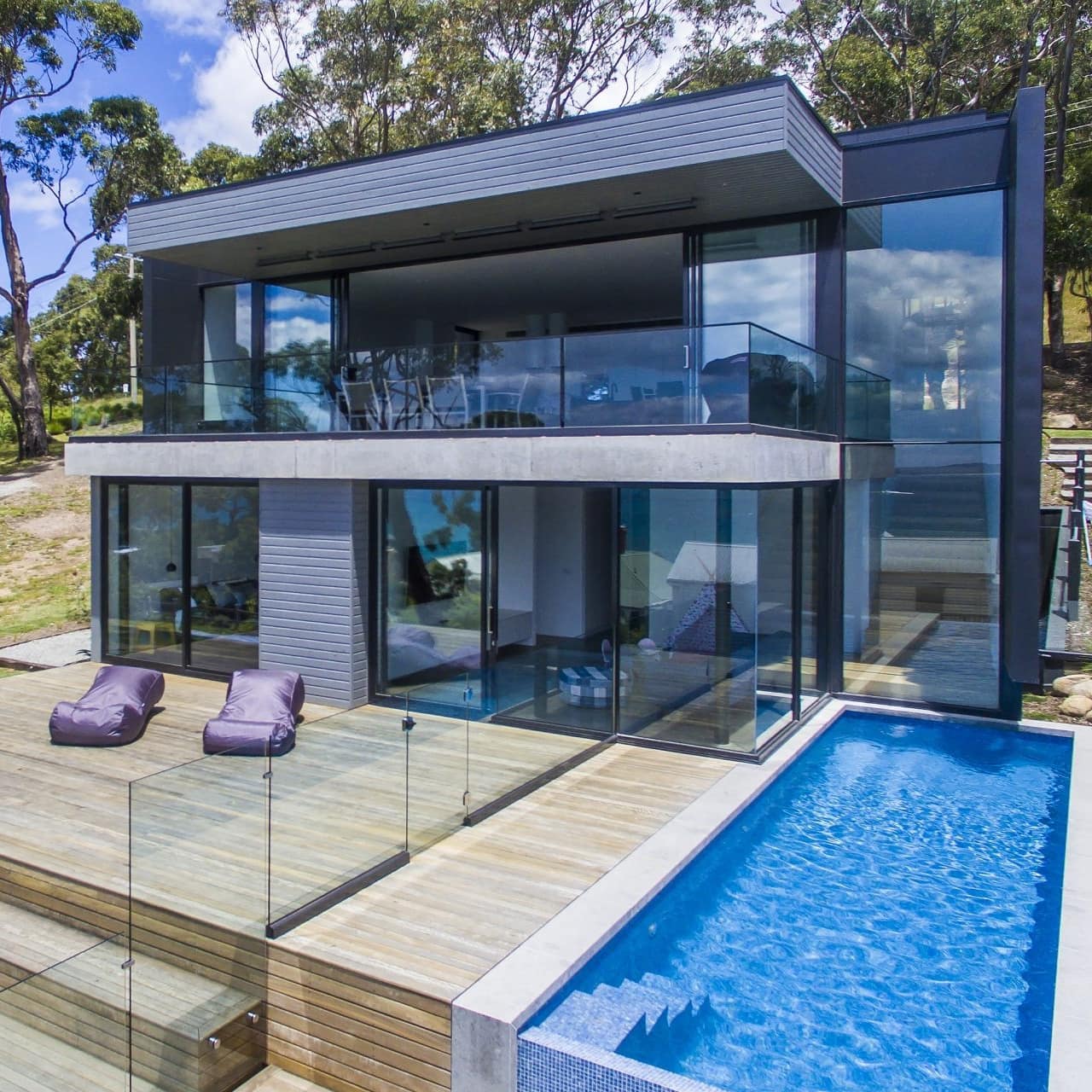 Modern two-storey home, grey brick siding, floor-to-ceiling windows, a wooden deck, and lap pool.