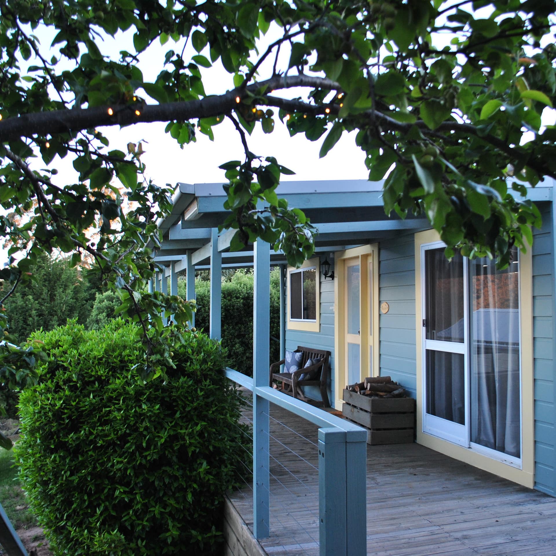 Cabin with blue exterior, porch and windows overlooking bush and mountains