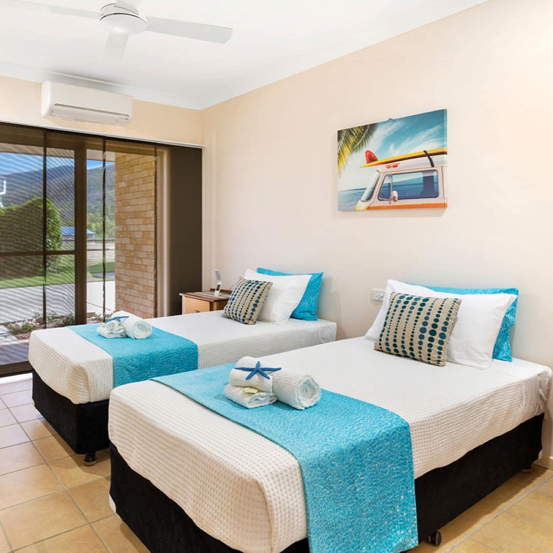 Bedroom with beige tile floors, white walls, two twin beds, white and blue bedding, nautical decor, sliding glass doors.