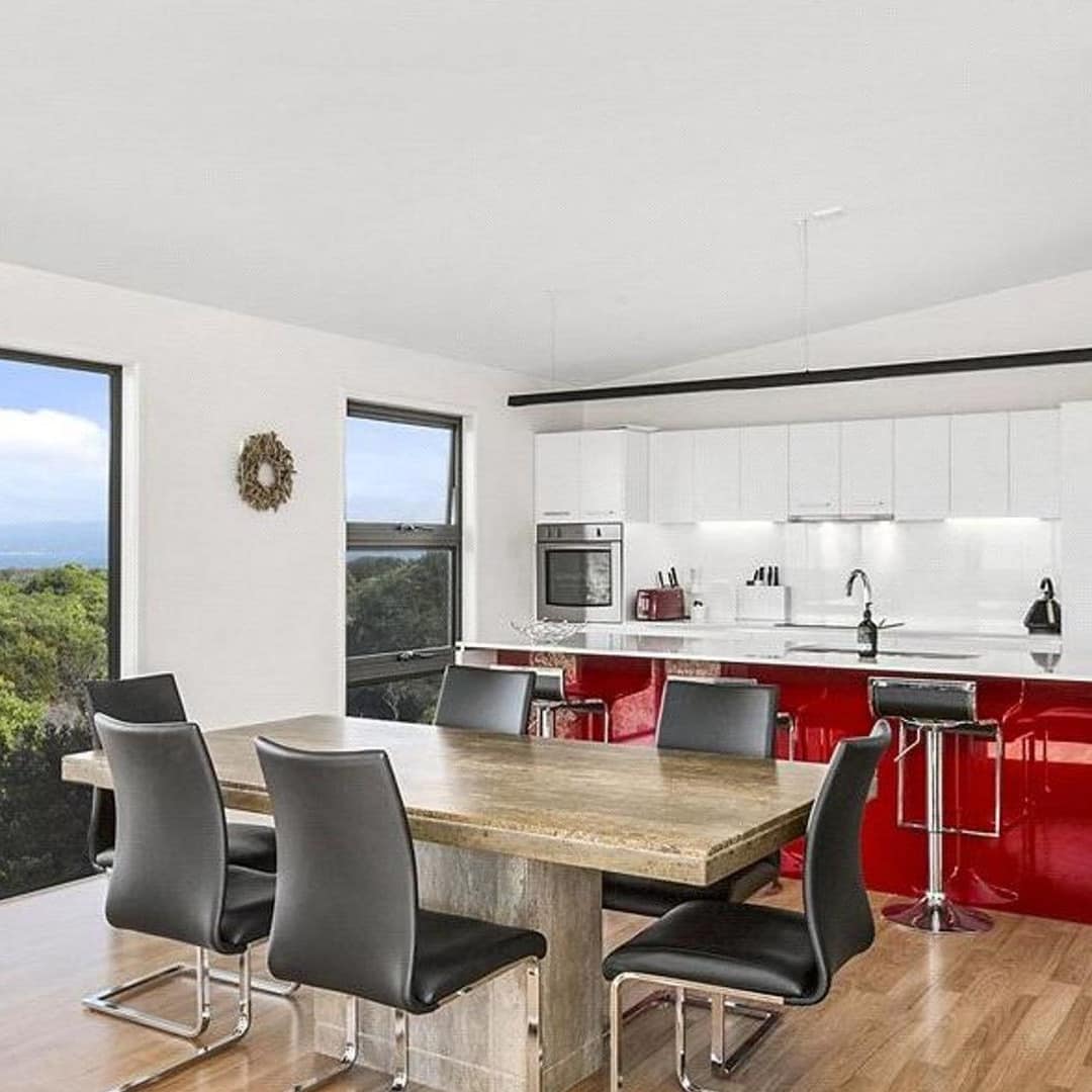 Open kitchen and dining room with hardwood floors, tall windows with nature views, modern kitchen, wooden dining set.