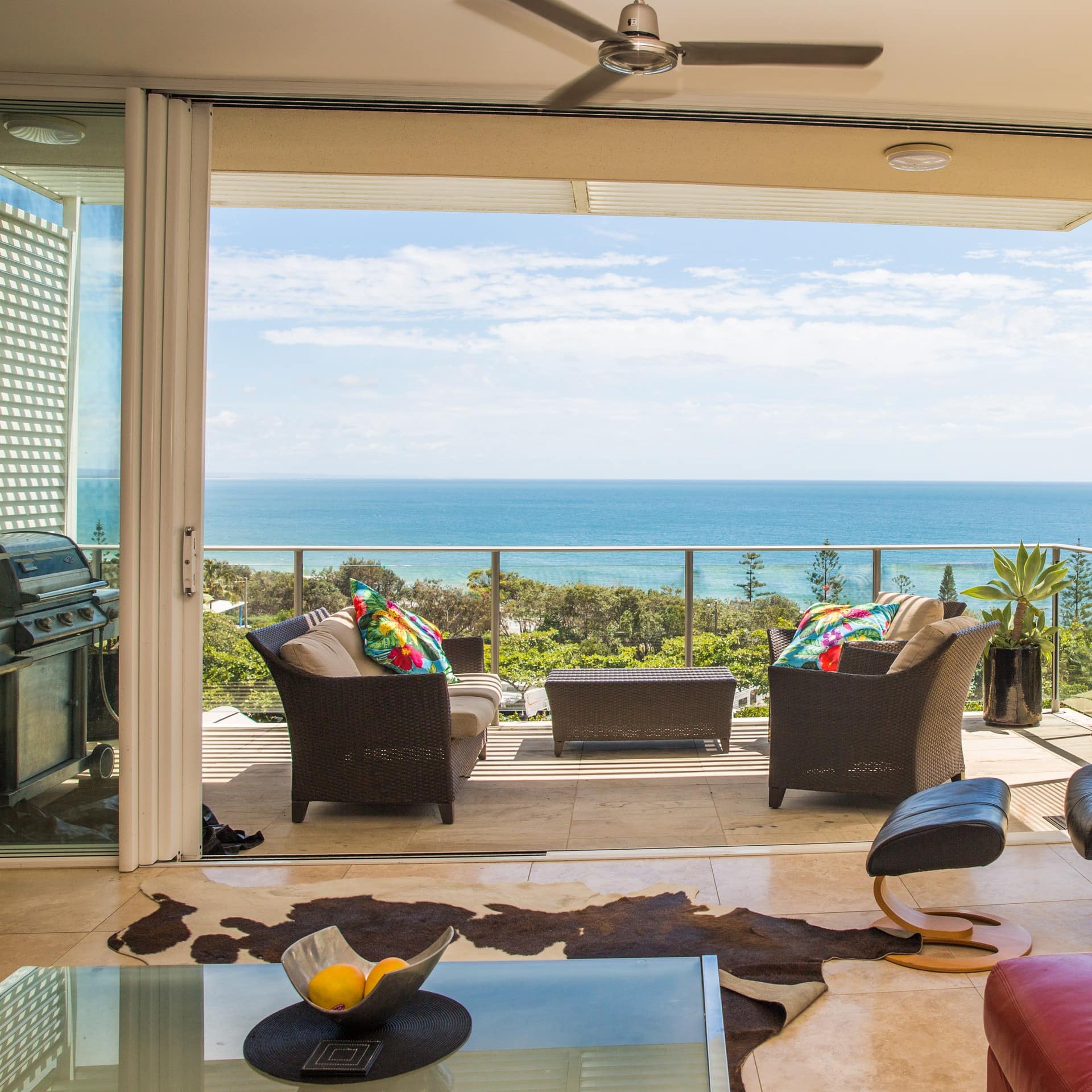 Living room with beige tile floors, a black leather chair, cowhide rug, and attached balcony with ocean views.