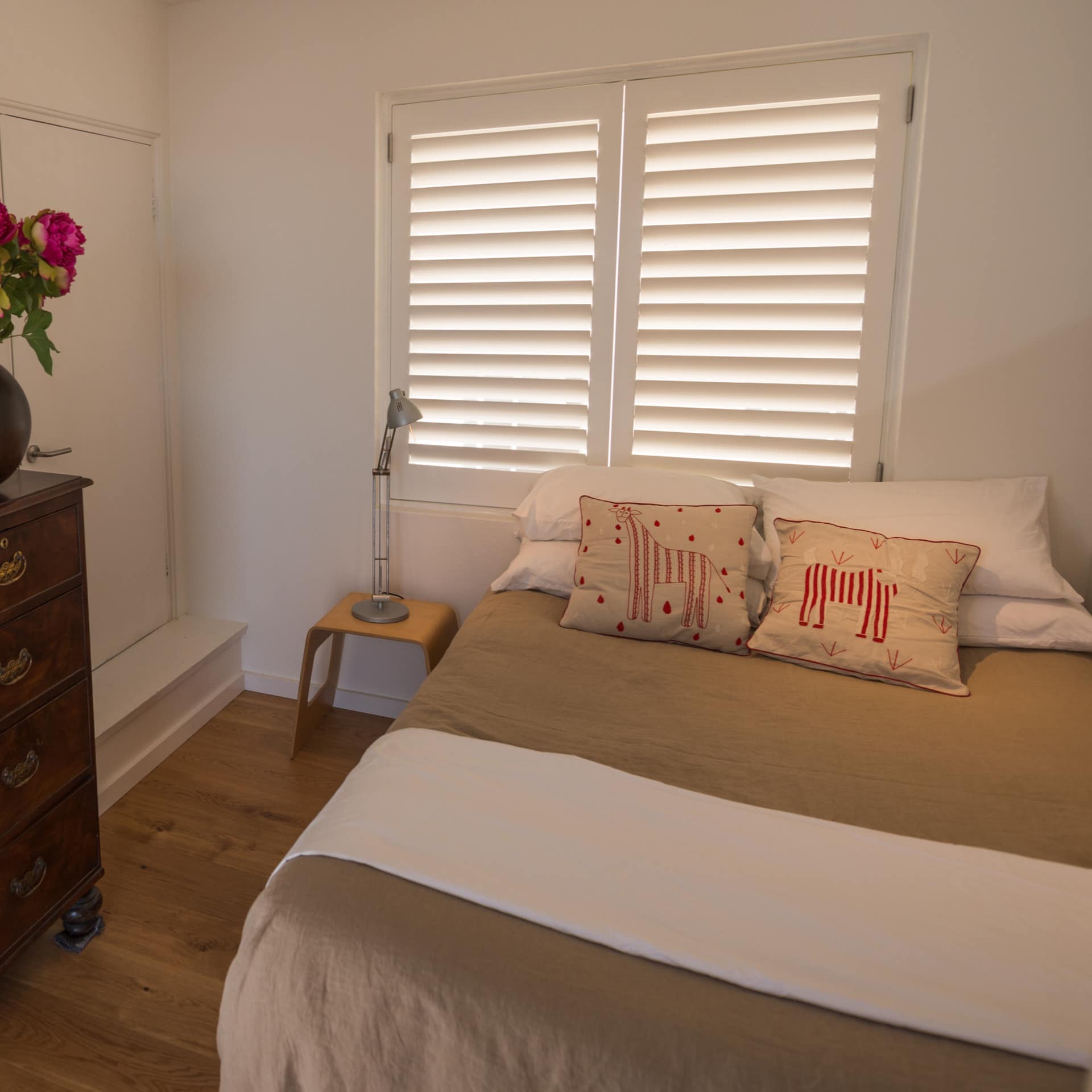 Bedroom with hardwood floors, a king size bed, tan and white bedding, and an antique dresser.