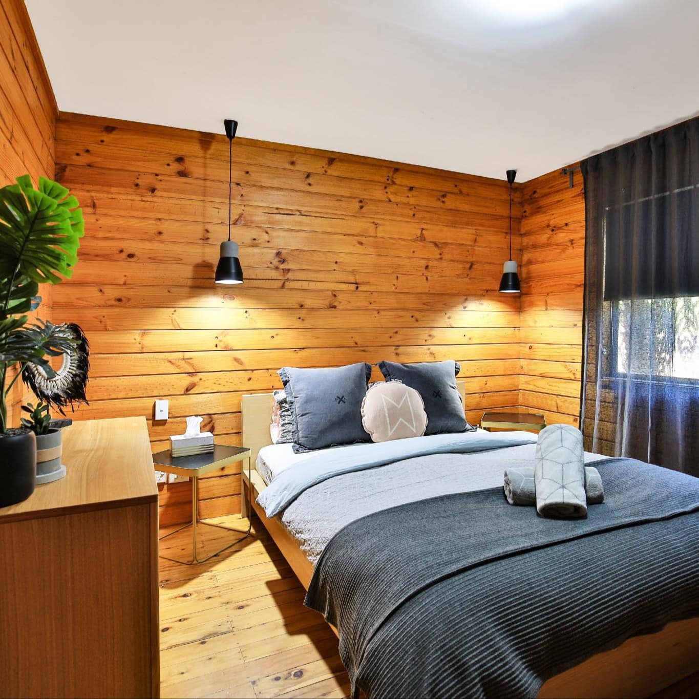 Bedroom with wood panelled walls, hardwood floors, queen size bed, blue and grey linen, grey window curtains.
