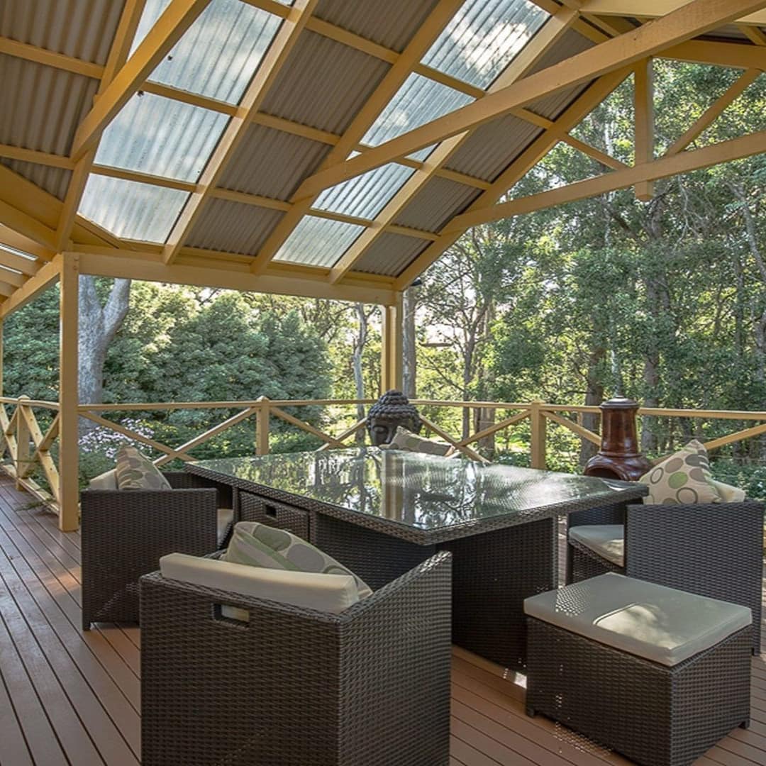 Large deck with barbecue, dining table and comfortable furniture covered by uniquely architectured roof with view of trees