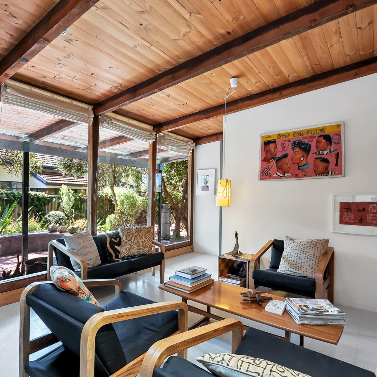 Modern living room with grey tile floors, contemporary wooden furniture, floor to ceiling windows with views of lush patio.