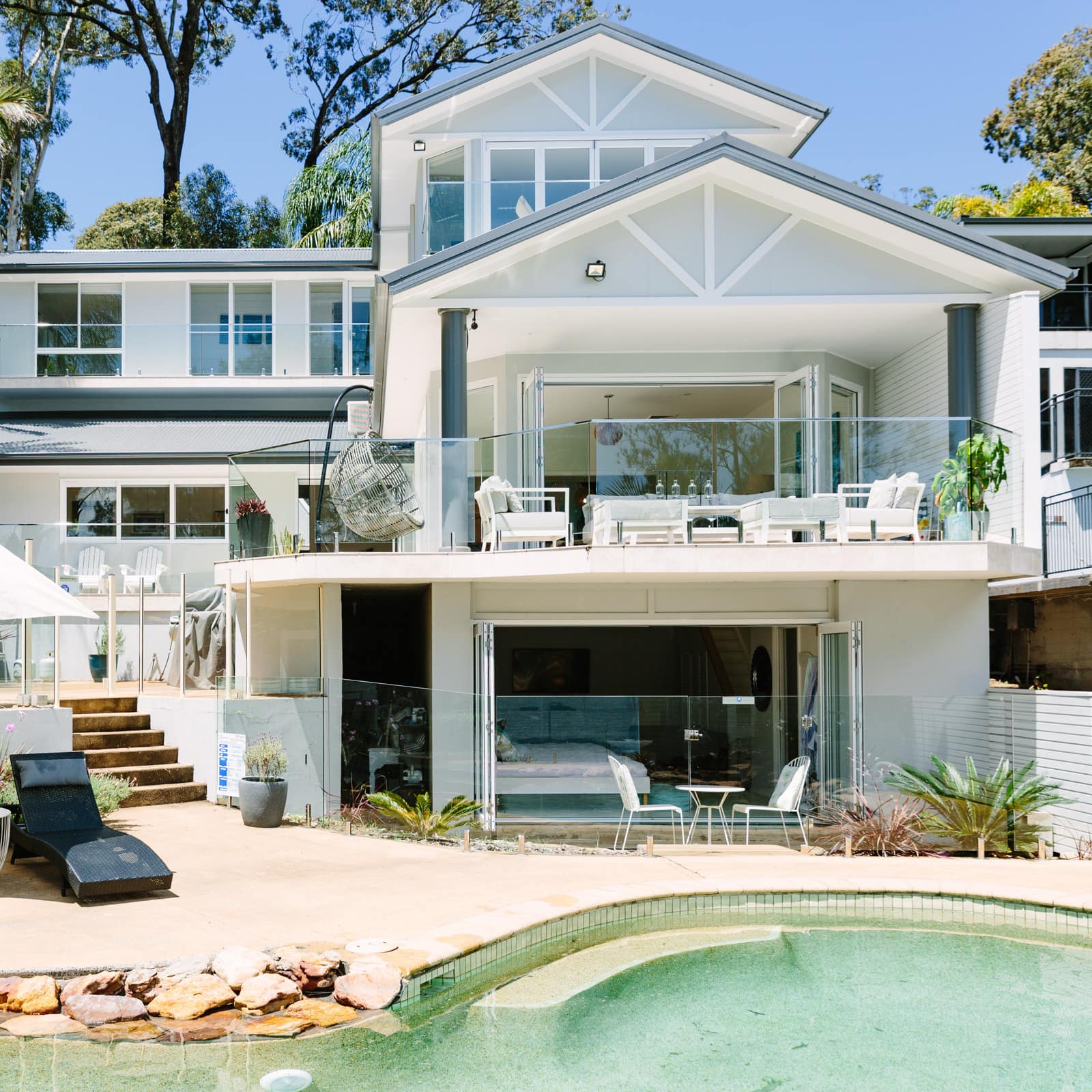 Exterior of modern, beach home, two patio areas, balcony overlooking a private pool with natural stone waterfall.