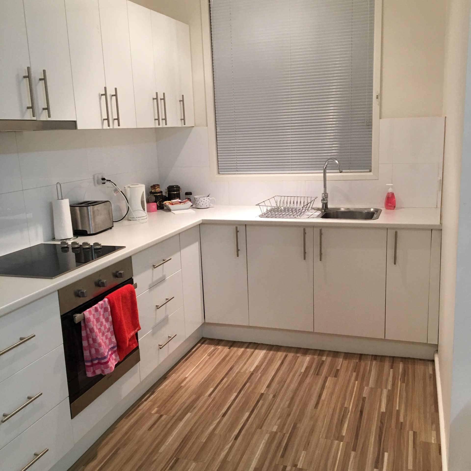 All-white kitchen with clean edges, high ceiling, minimalistic design, smooth-top stove and wooden floors