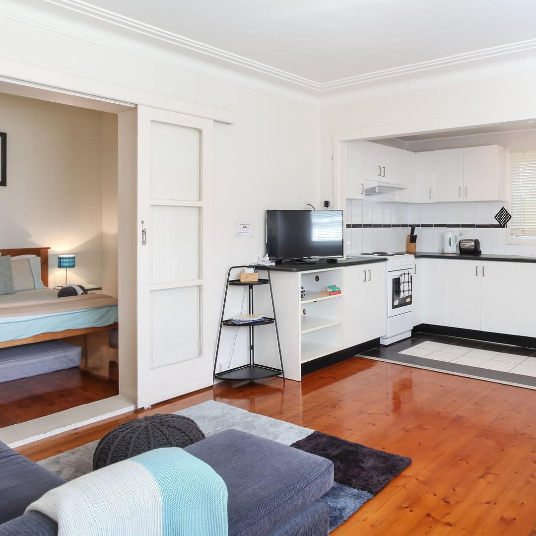 Open living room and kitchen with sliding doors to the bedroom, hardwood floors, white walls, black and blue furnishings.