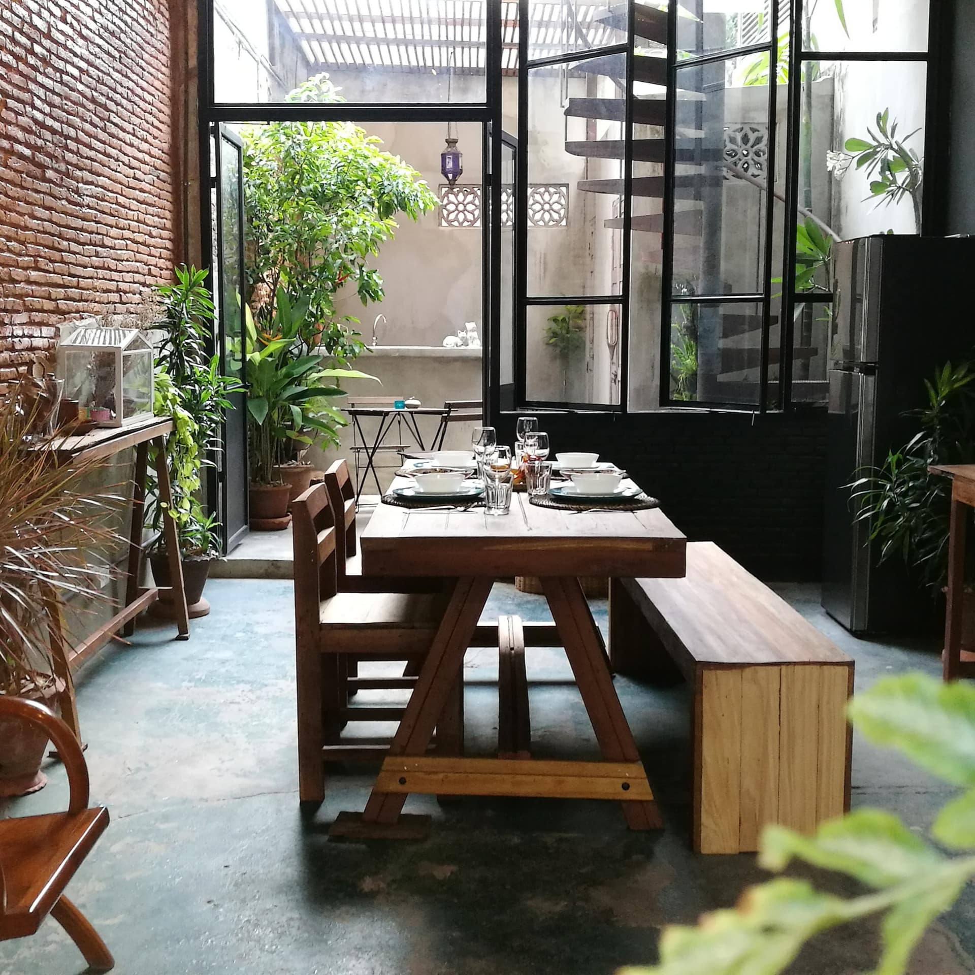 Rustic studio space with exposed brick walls, cement floors, wooden furniture, potted plants and an attached courtyard space.