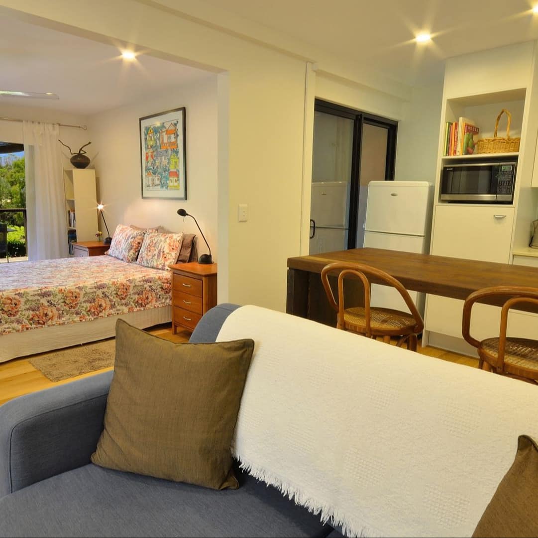 Studio space with a modern kitchen, wooden island, blue sofa, and a king size bed with floral bedding.