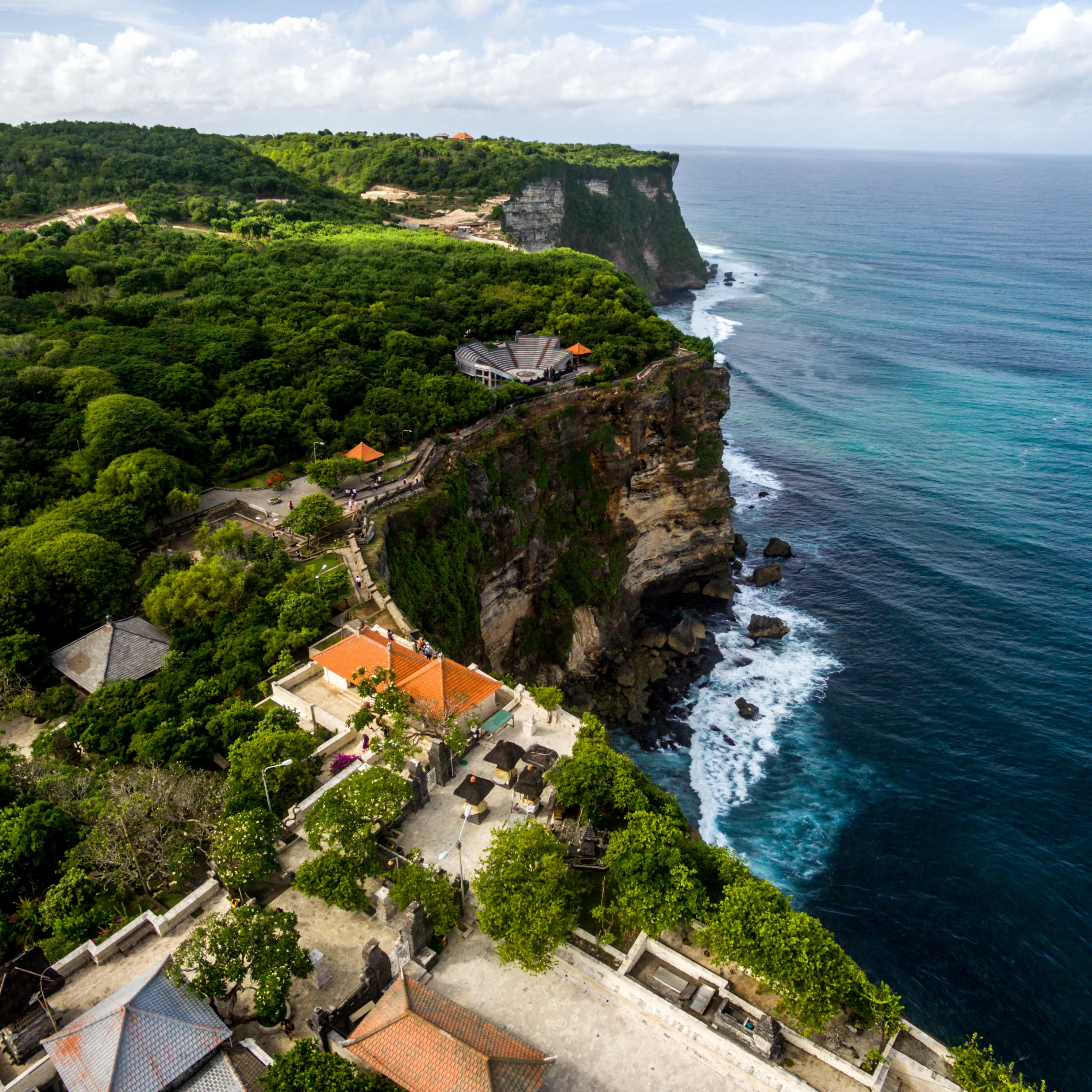 An aerial view of clifftop villas surrounded by lush green trees with a view of the turquoise ocean