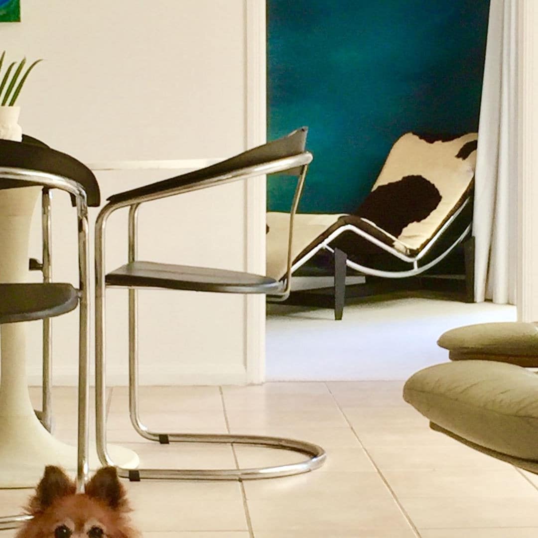 View of a dining room with white tile floors, white walls, a round dining set, a green chair, and a small dog.