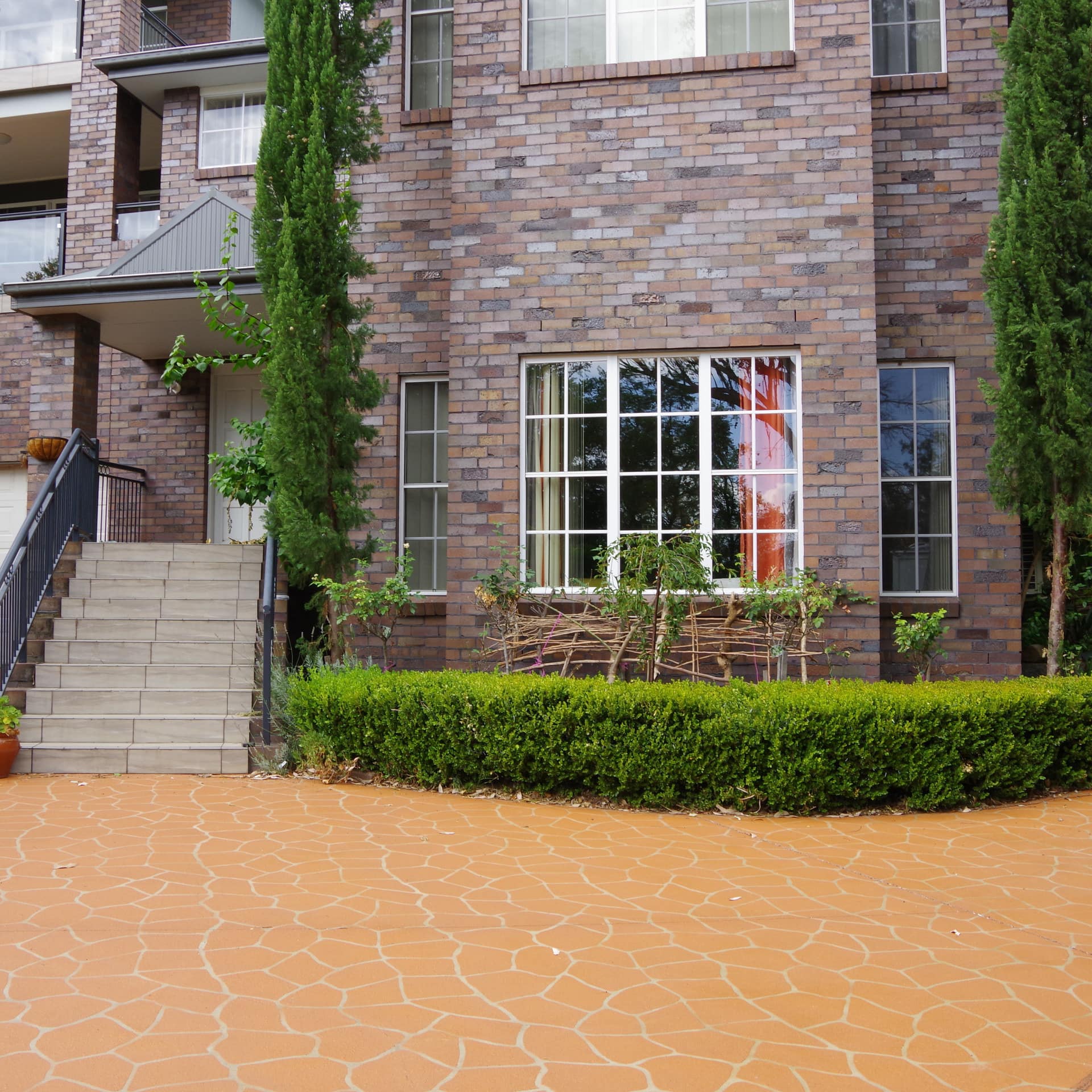 Exterior of brick apartment building with orange stone walkway, grey stone stairs, and green shrubbery and trees.