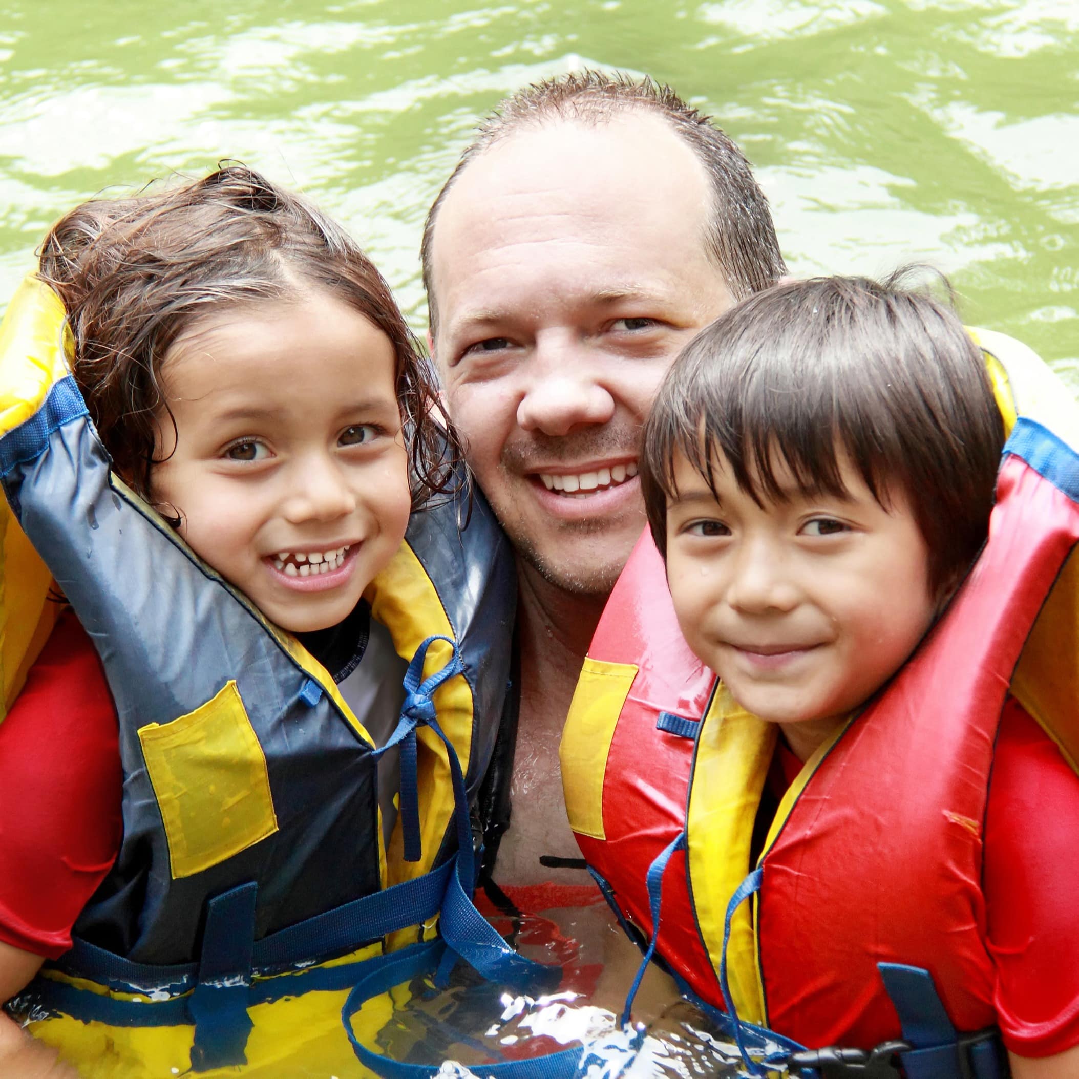 Father and two children with flotation devices having fun in water on a sunny day