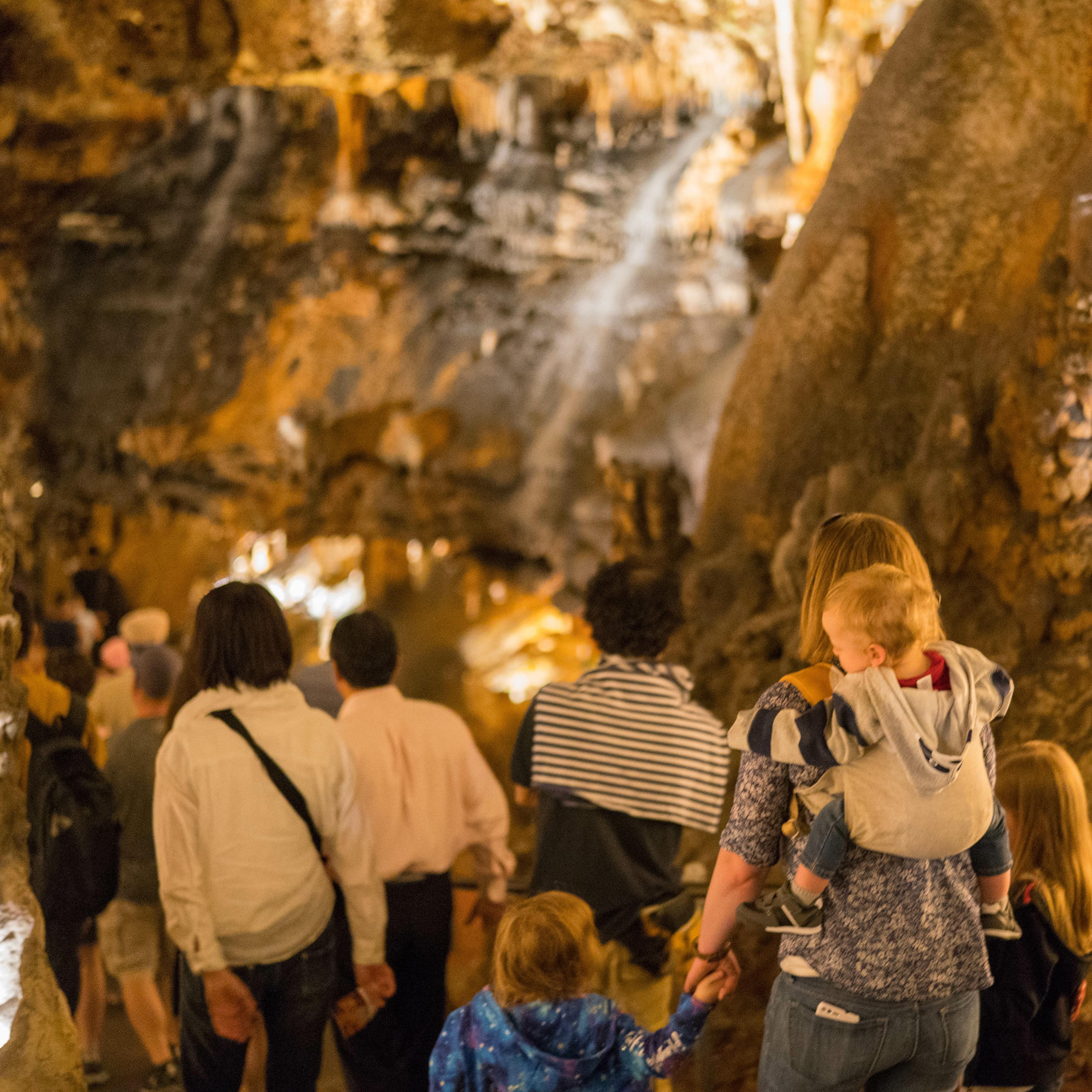 Group of tourists, including a mom with a baby on her back touring a cave