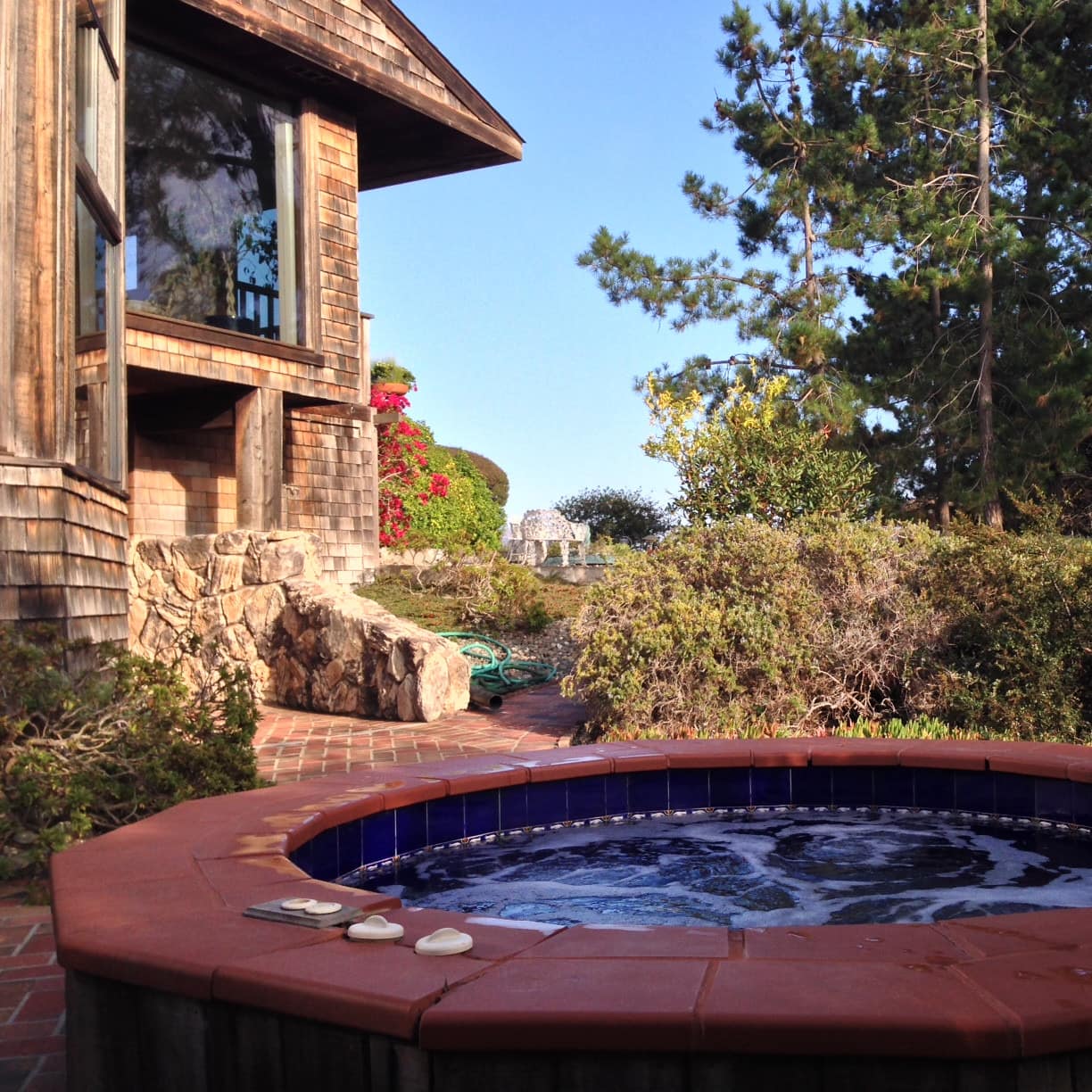View of a hot tub and a brick patio space next to a home with wood shingle siding.