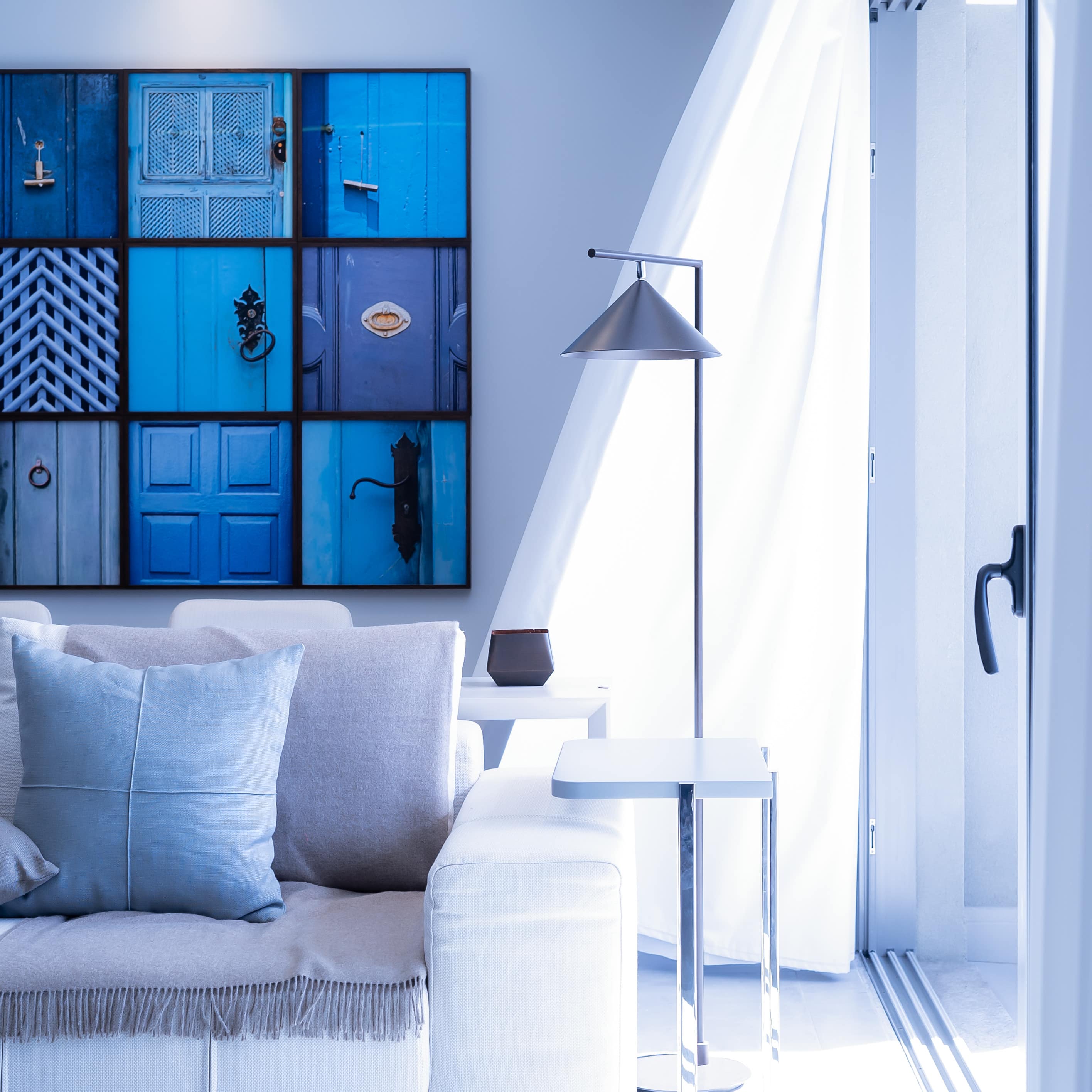 Interior of chic apartment with white leather sofa, blue photographic art, and sliding glass window to a balcony