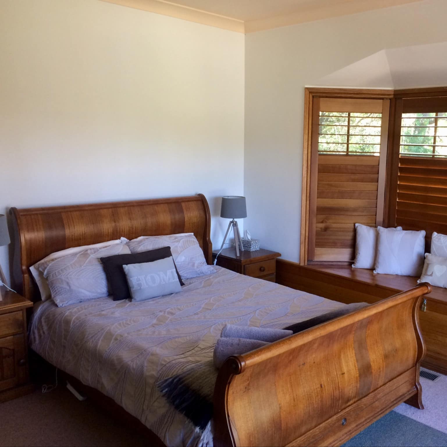 A bedroom with wooden sleigh bed, light-blue bedding and bay window with wooden window seat.